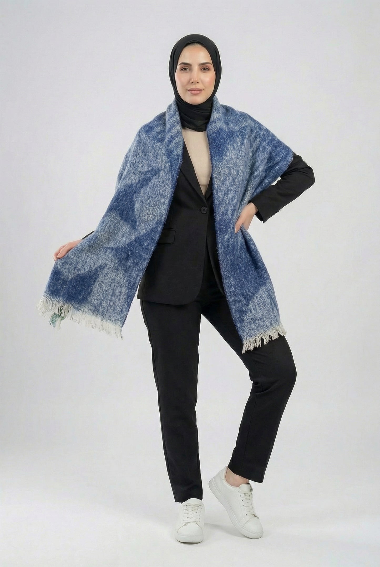 Woman wearing a blue patterned shawl over a black outfit on a white background