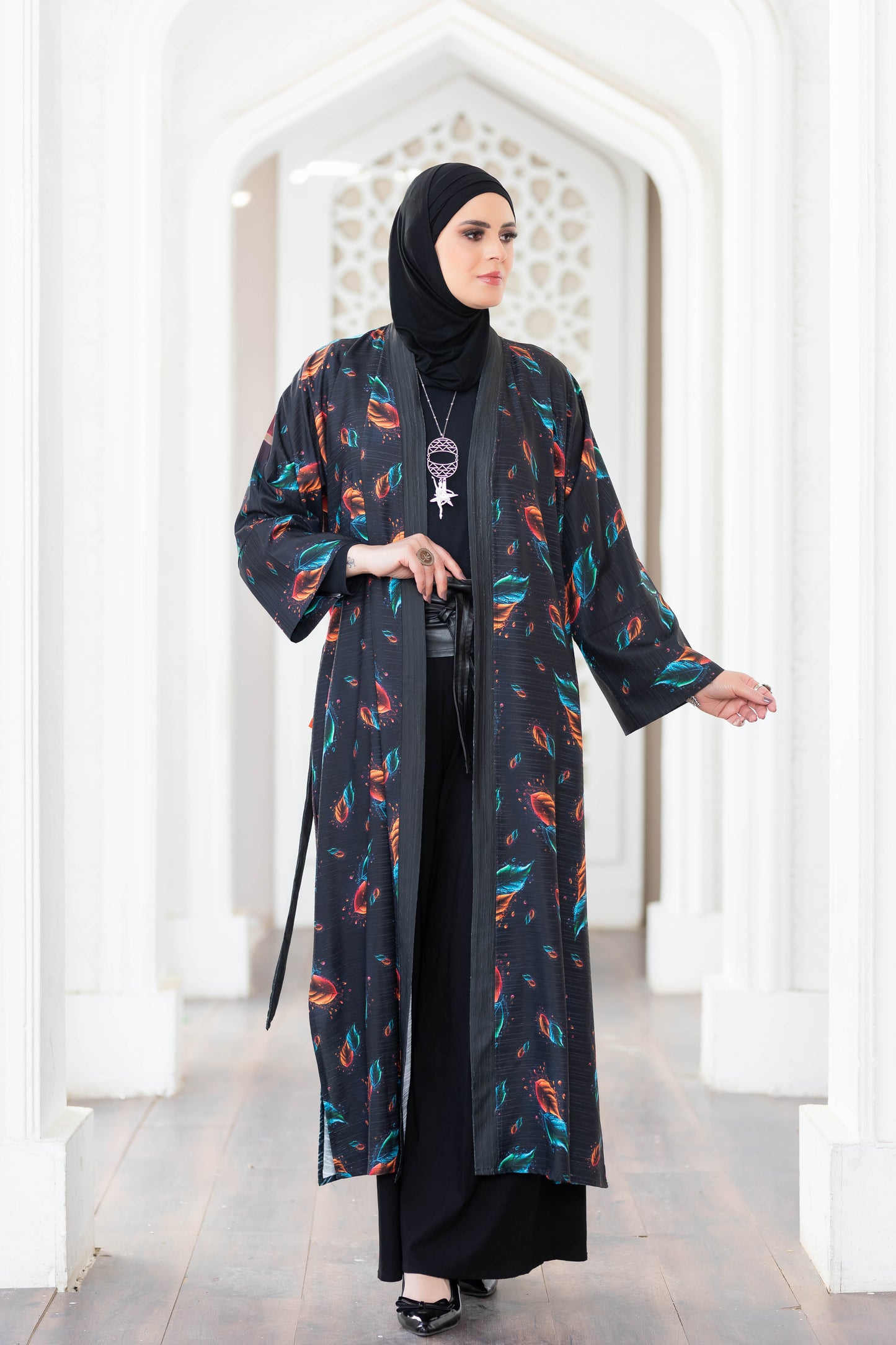 Ornate digital print kimono with vibrant feather motifs worn by a woman against a white architectural background at Satr store.