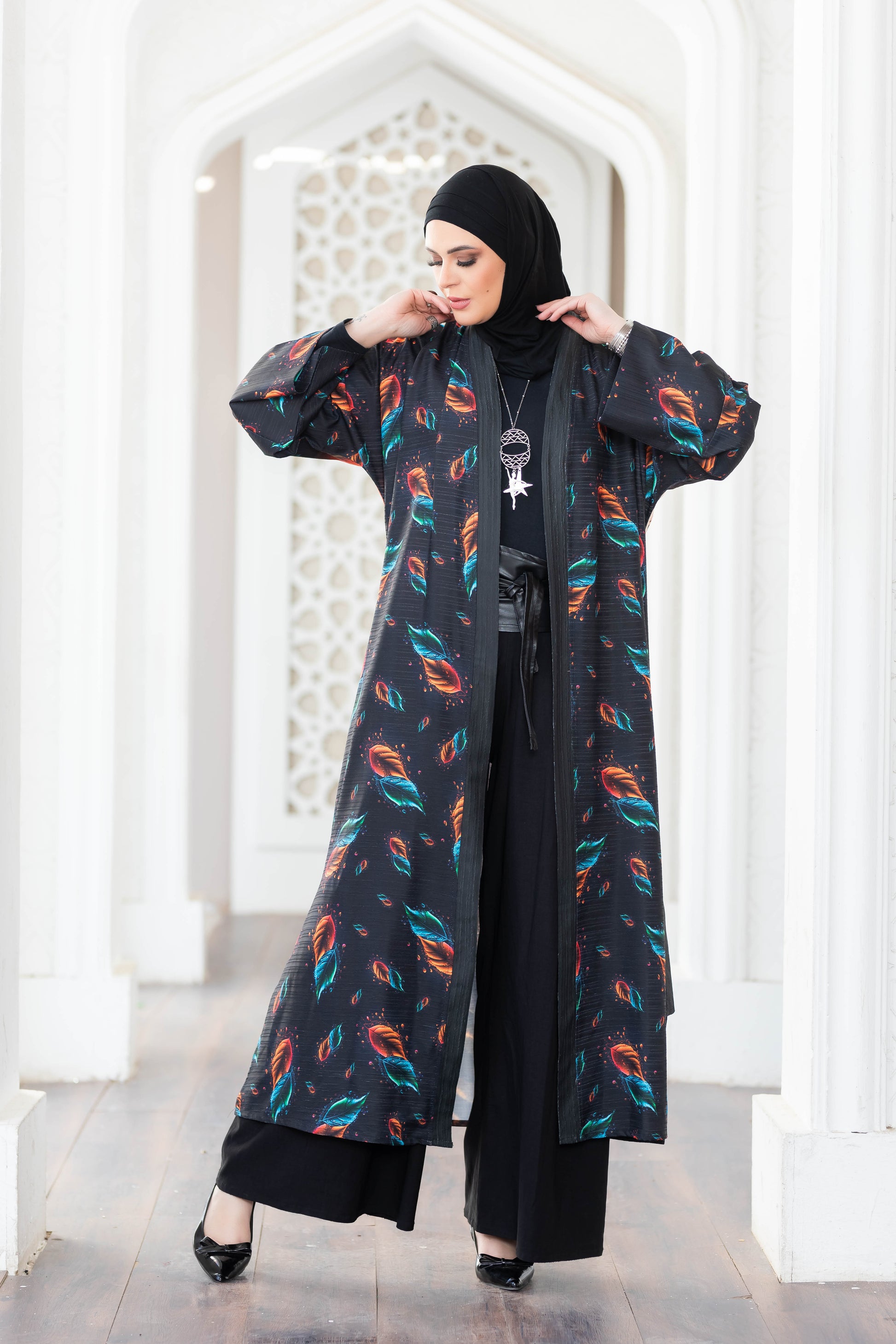 Colorful feather-patterned digital print kimono with long sleeves and a draped silhouette, worn by a person standing in a bright, architecturally detailed setting.