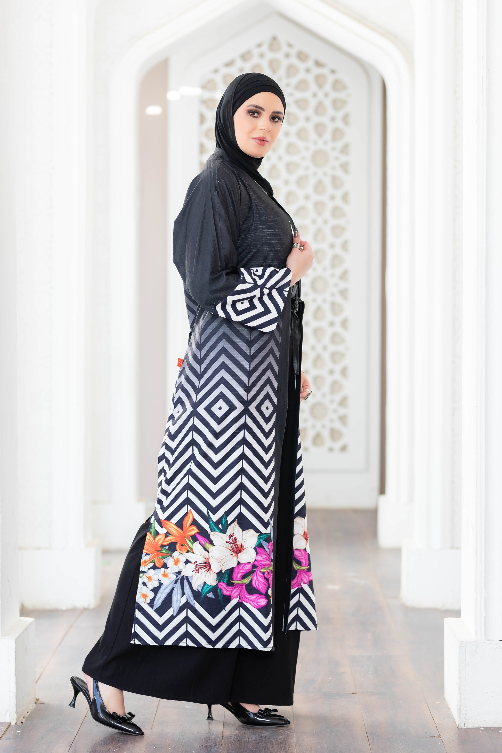 Elegant black and white patterned kimono with floral accents on a female model standing in an arched white doorway.
