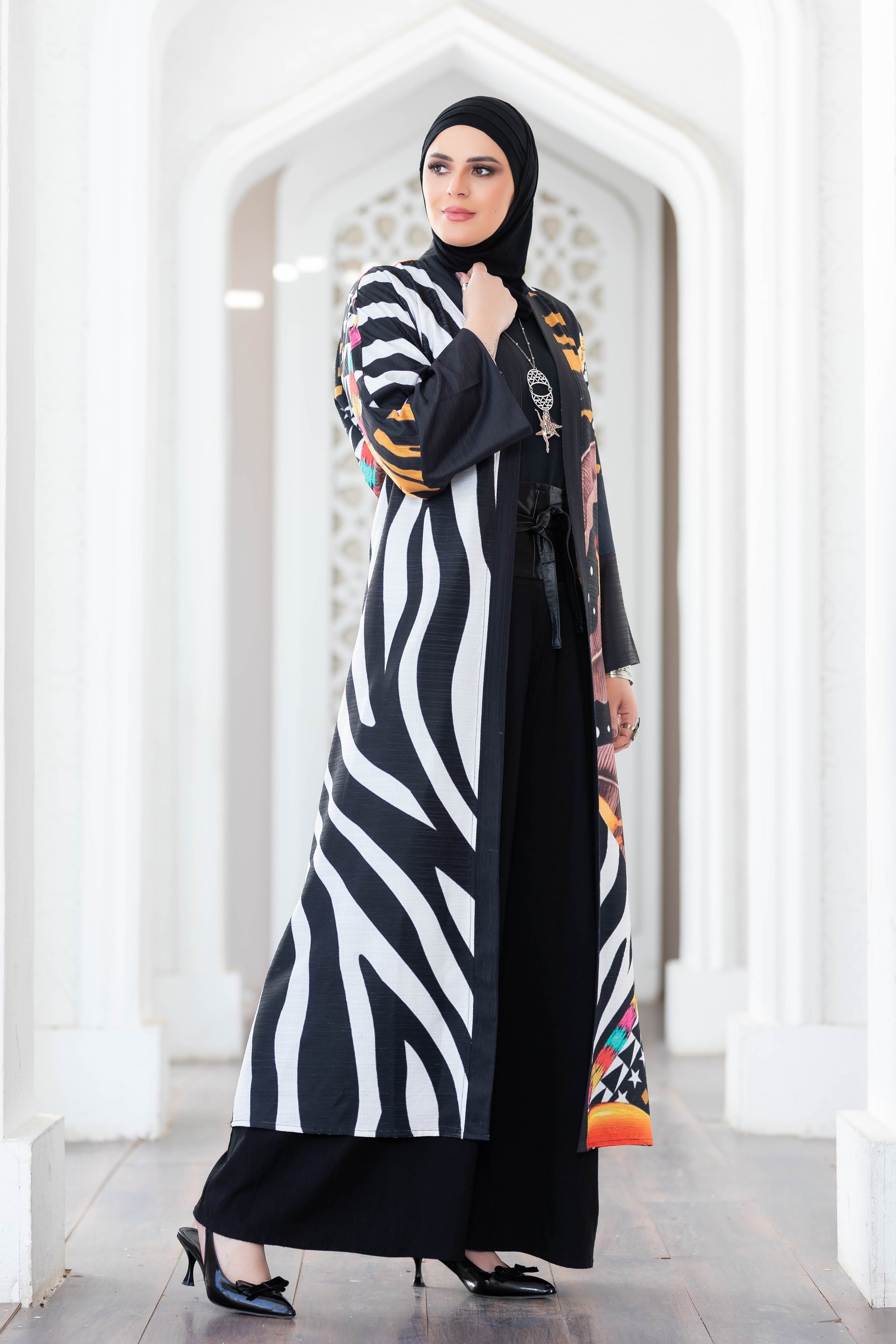 Elegant striped kimono with vibrant floral accents, worn by a woman in traditional Islamic dress, standing in an arched doorway.