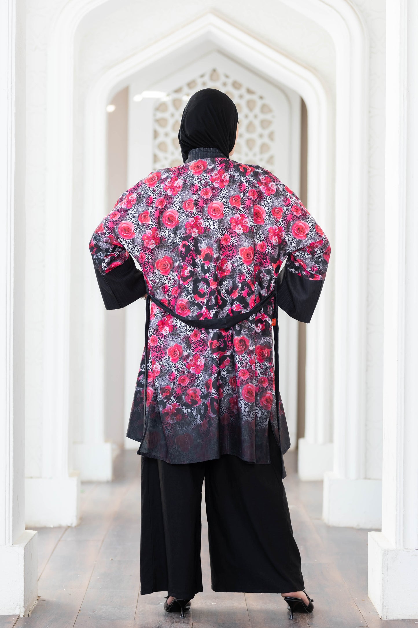 Vibrant floral short kimono with intricate digital print, contrasting black accents, and a stylish sash waist, displayed in a striking architectural setting.