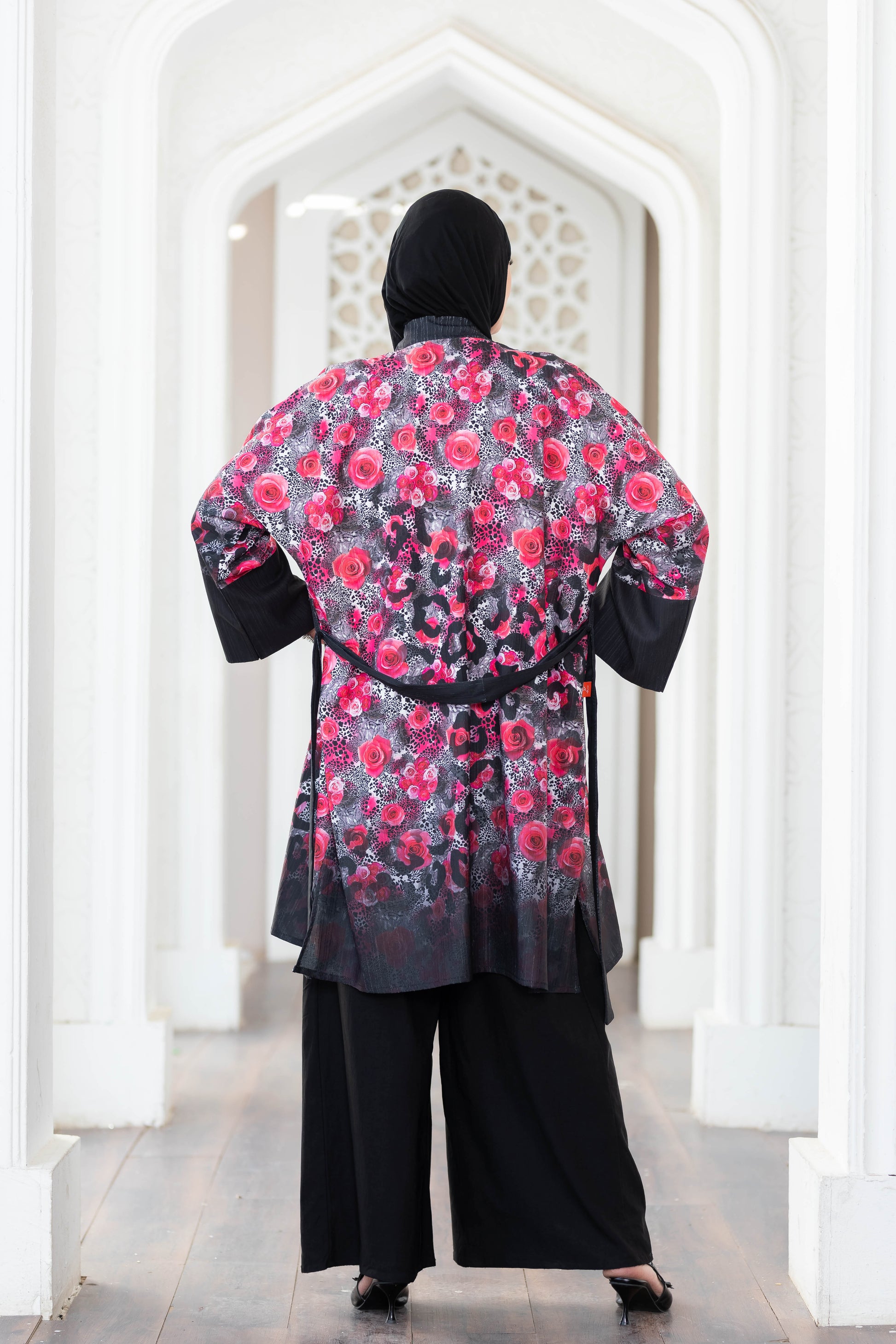Vibrant floral short kimono with intricate digital print, contrasting black accents, and a stylish sash waist, displayed in a striking architectural setting.