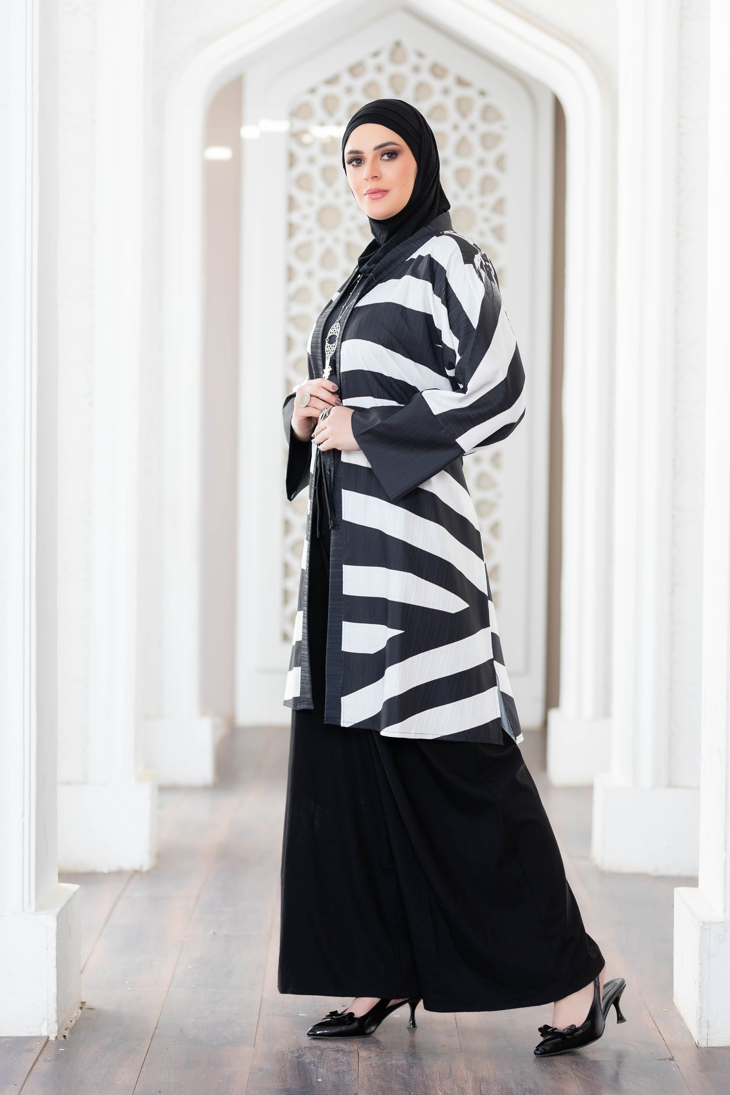 Stylish zebra-patterned short kimono with a flowing black skirt worn by a woman with a hijab in a decorative architectural setting.
