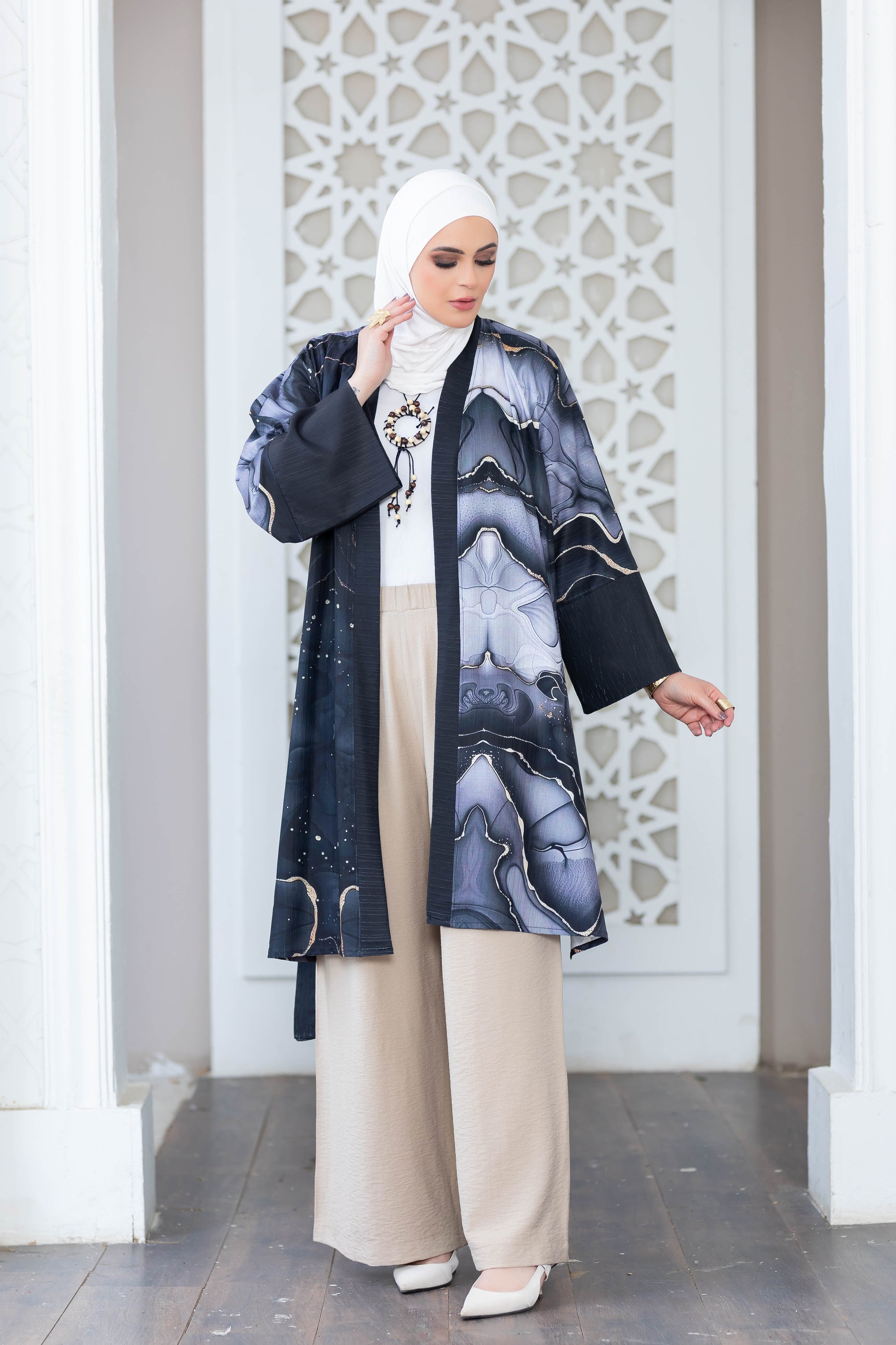 Elegant printed kimono with intricate floral patterns and contrasting colors, worn by a woman with a hijab as she stands in front of an ornate white architectural backdrop.