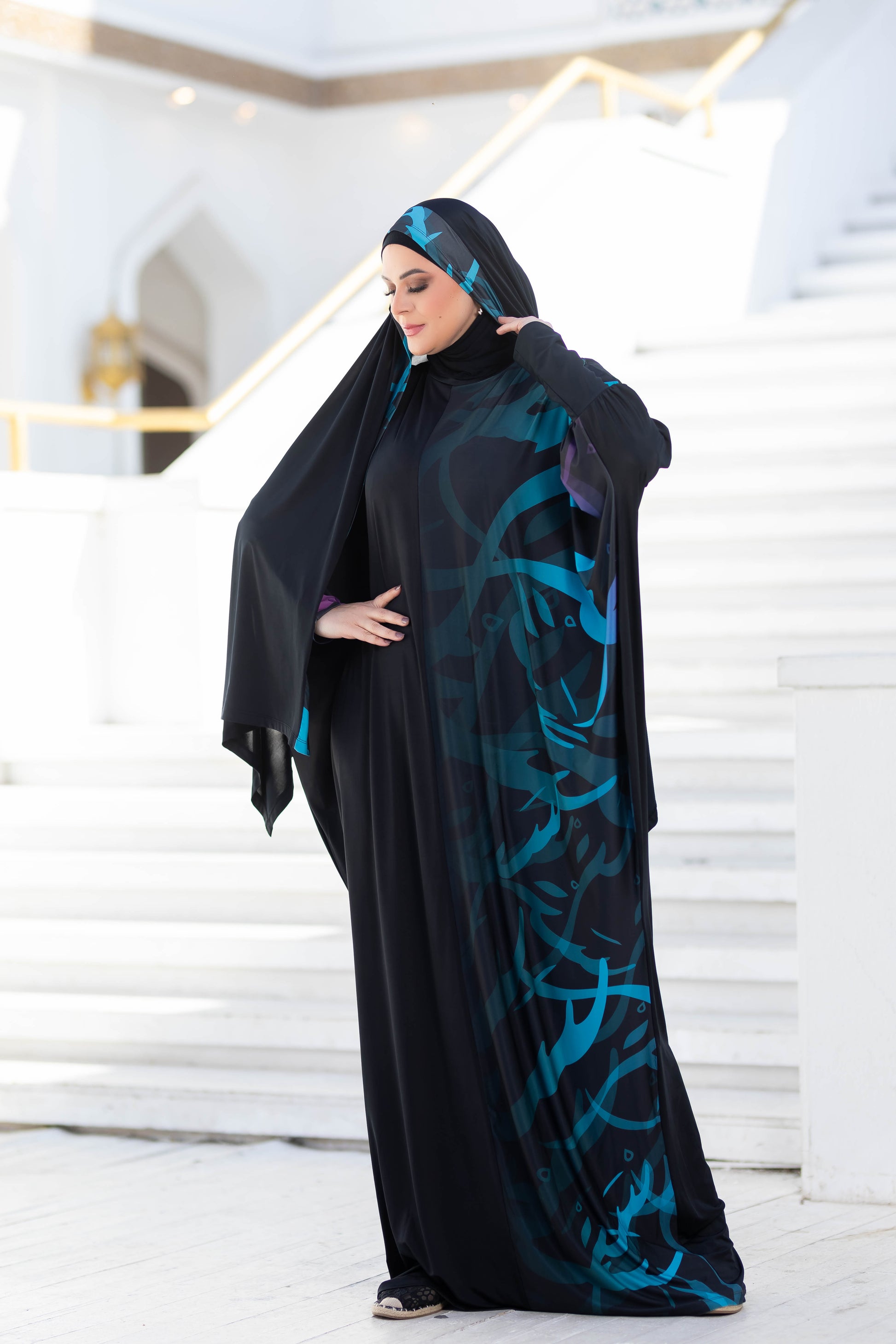 Modest Isdal 777177 - Elegant Islamic-inspired abaya with abstract blue patterns, worn by a woman standing in a bright, open space.