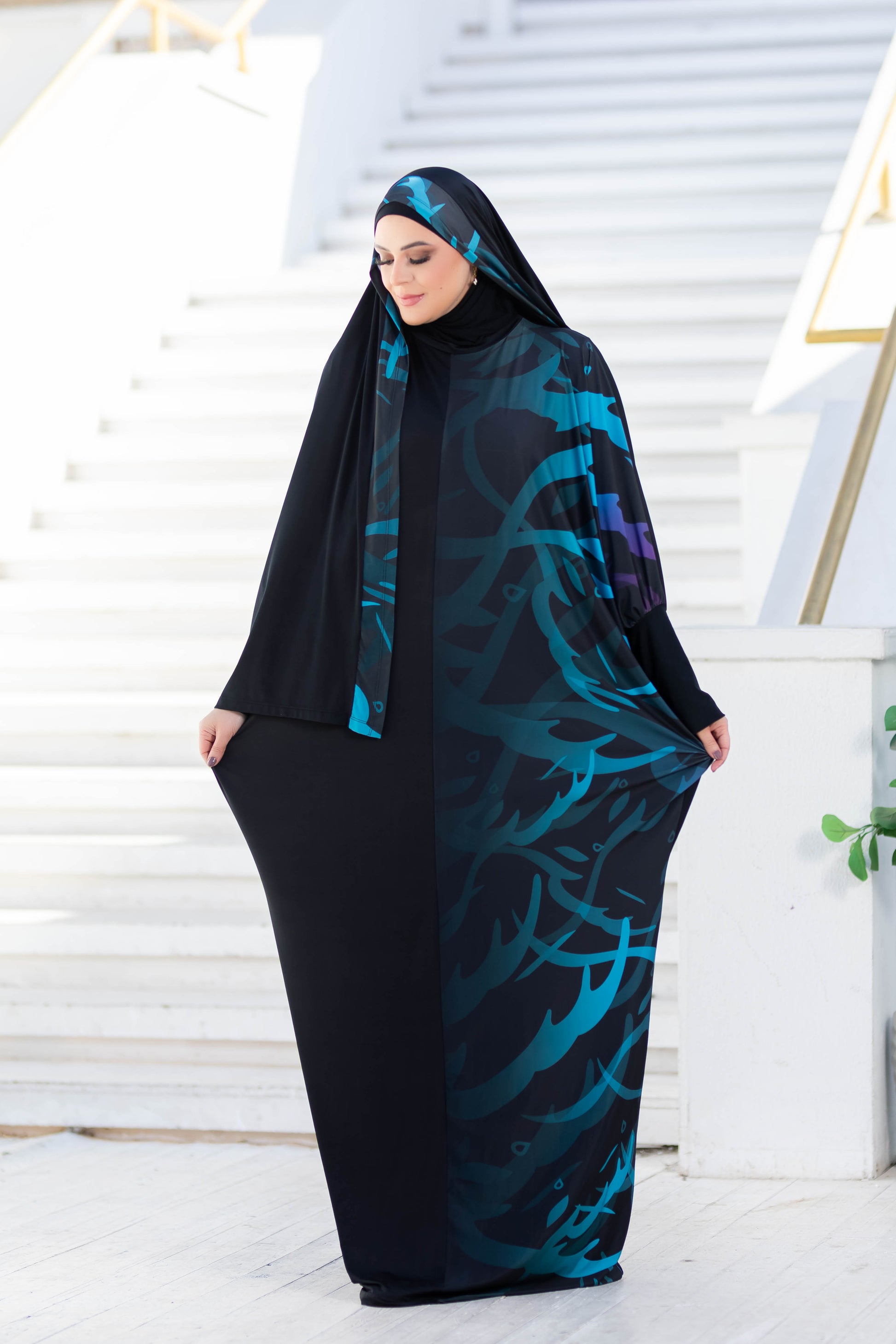 Modest Isdal 777177 ESDAL in patterned black and teal full-length dress, worn by a woman with head covered, standing on steps