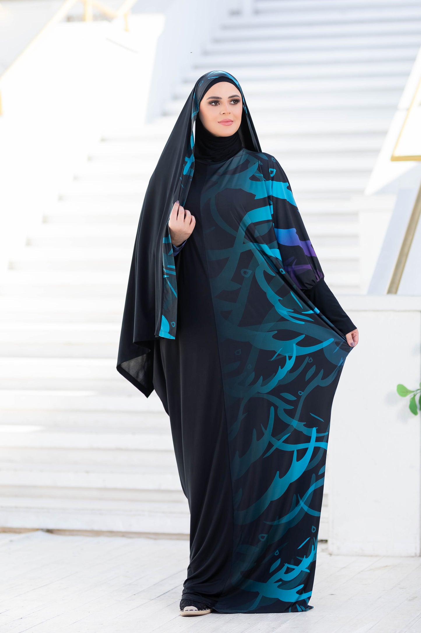 Modest Isdal 777177: Elegant Islamic fashion attire with abstract floral print in teal and purple tones, worn by a woman standing on steps.