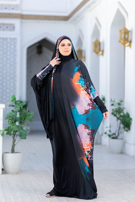 Modest Isdal 777179 ESDAL - Elegant black abaya with vibrant floral print accents, worn by a woman indoors with traditional Middle Eastern decor.