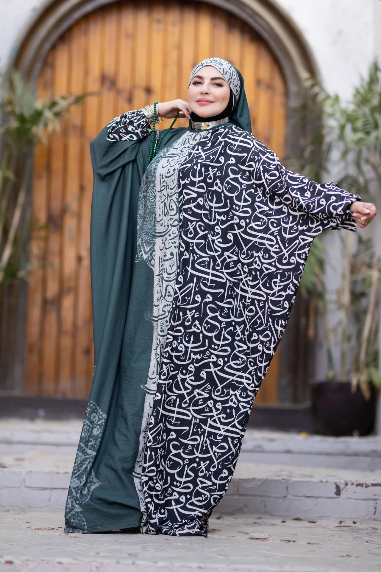 Woman wearing a black and white patterned abaya with a green hijab, standing outdoors.