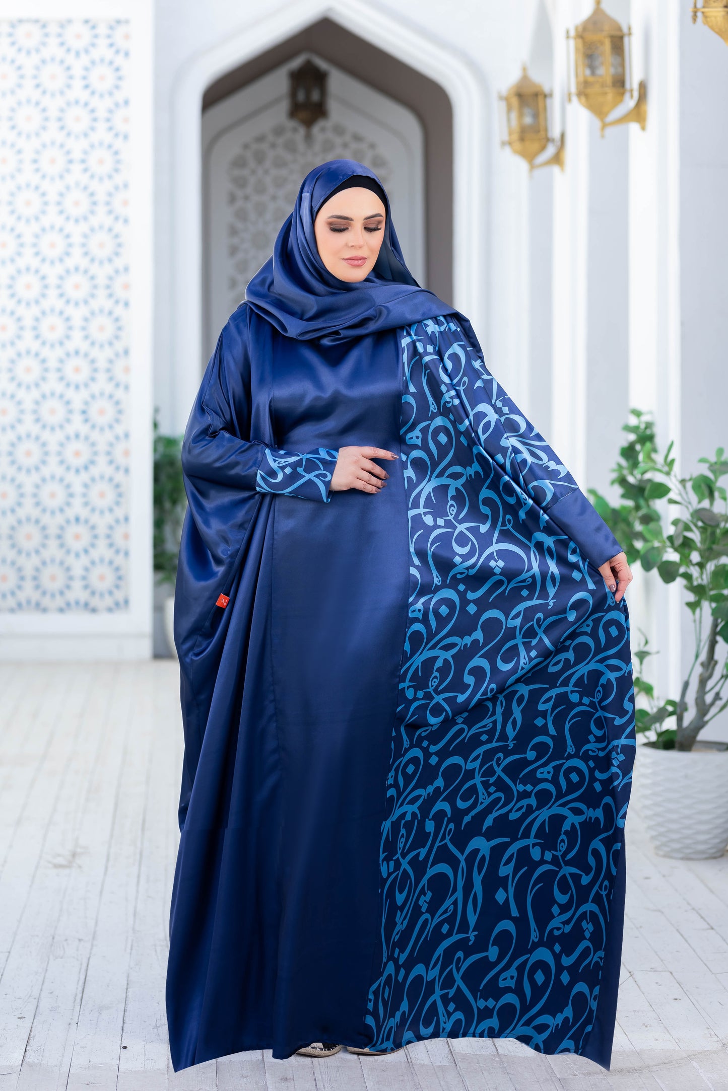 Modest navy blue satin Isdal 777189 dress with intricate embroidered patterns, worn by a woman standing in a traditional architecture setting.
