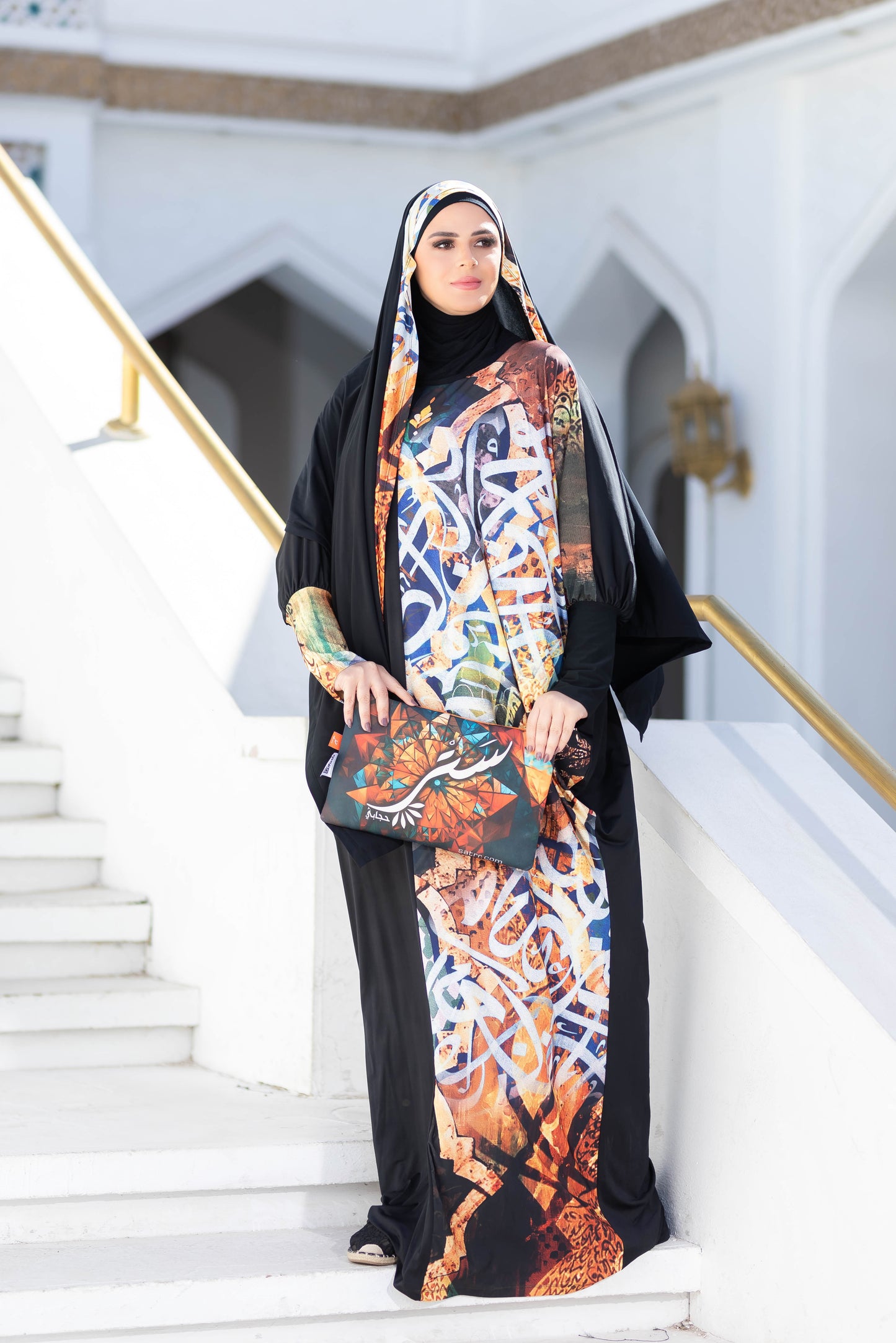 Elegant Islamic attire, colorful patterned dress, flowing black hijab, modern yet modest fashion, woman standing on steps.