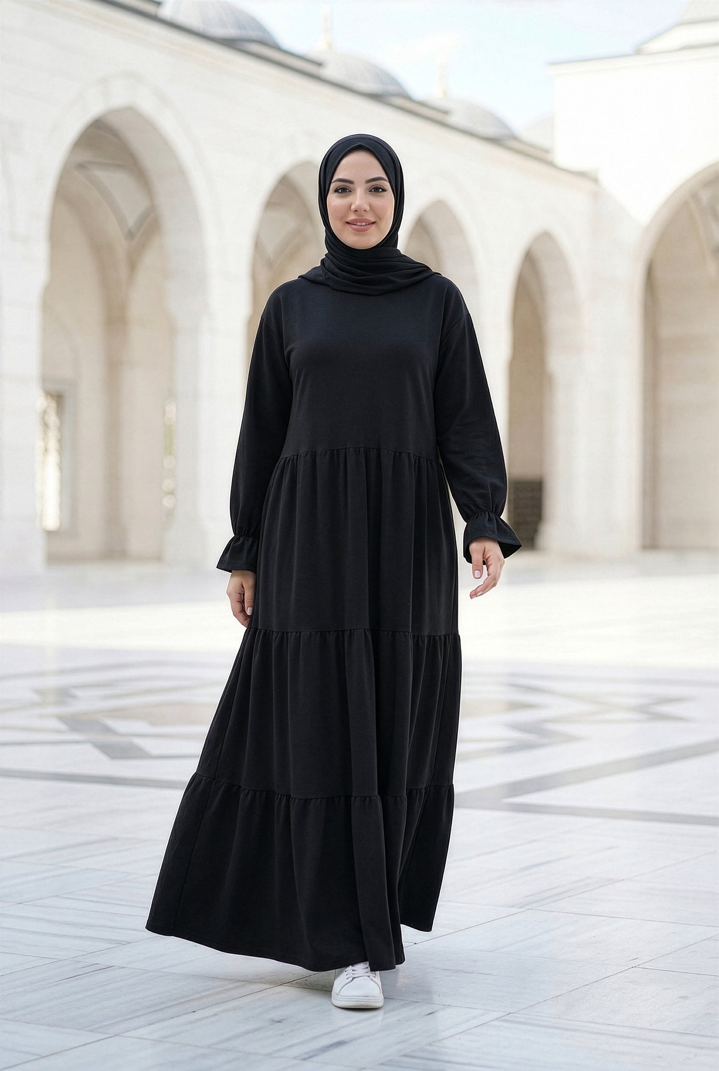 Model wearing Black Soft Flow Isdal with flowing tiered silhouette in an elegant outdoor courtyard
