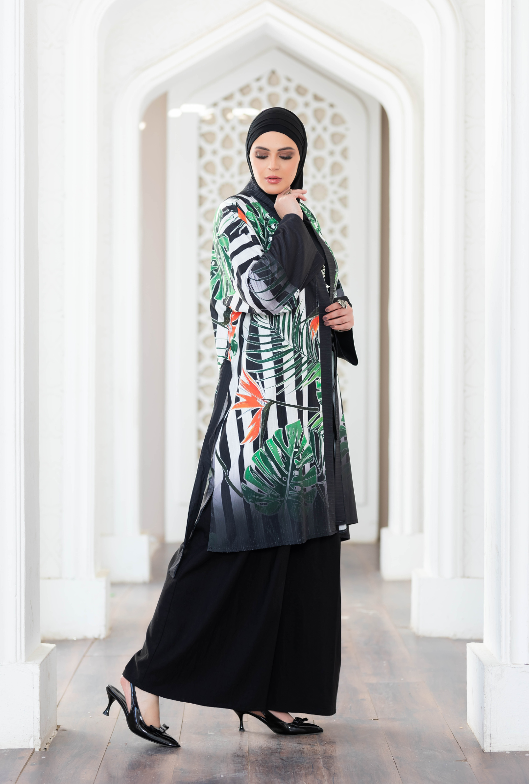 Woman wearing stylish long printed kimono with black abaya and heels in front of ornate architecture