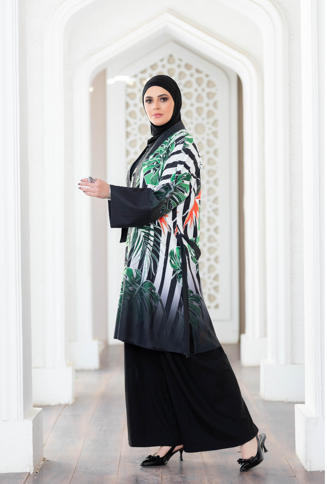 Vibrant printed short kimono with tropical leaf pattern, worn by a woman in traditional Islamic dress, standing in an ornate archway.