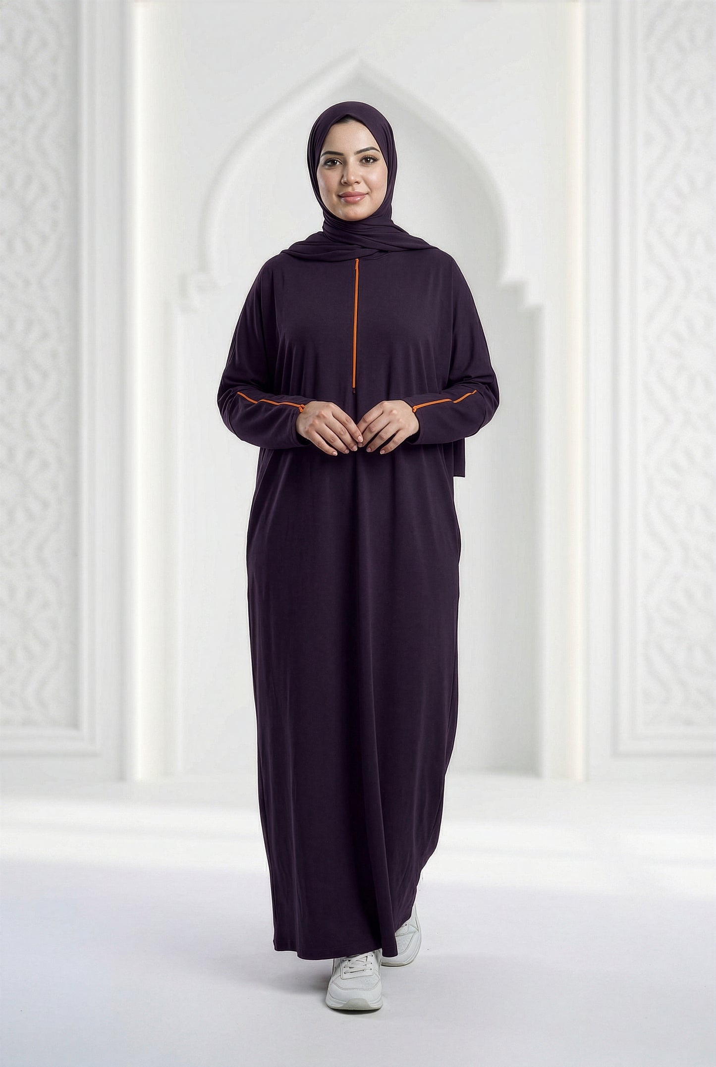 Woman wearing a deep plum Oumra Isdal with embroidered front and sleeve detailing, modest flowing silhouette, in an elegant indoor archway setting