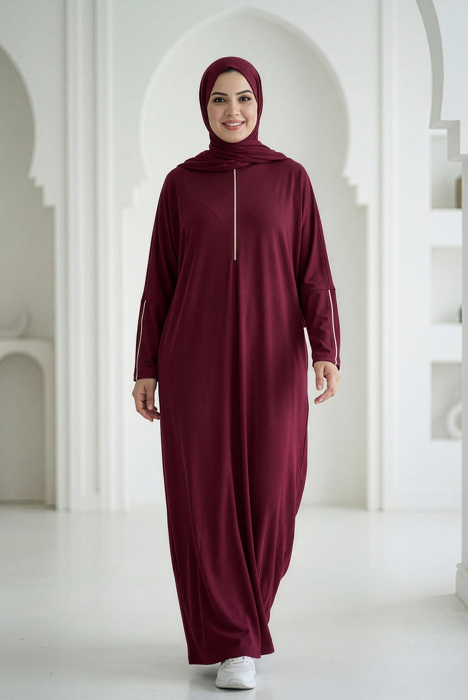 Woman wearing a burgundy abaya in a white architectural setting