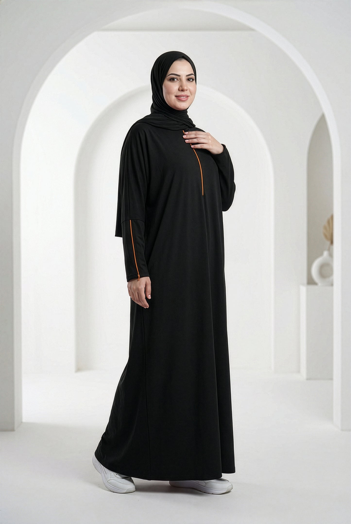 Woman wearing a black Oumra Isdal with embroidered sleeve and front detailing, modest flowing silhouette, standing in an elegant indoor archway