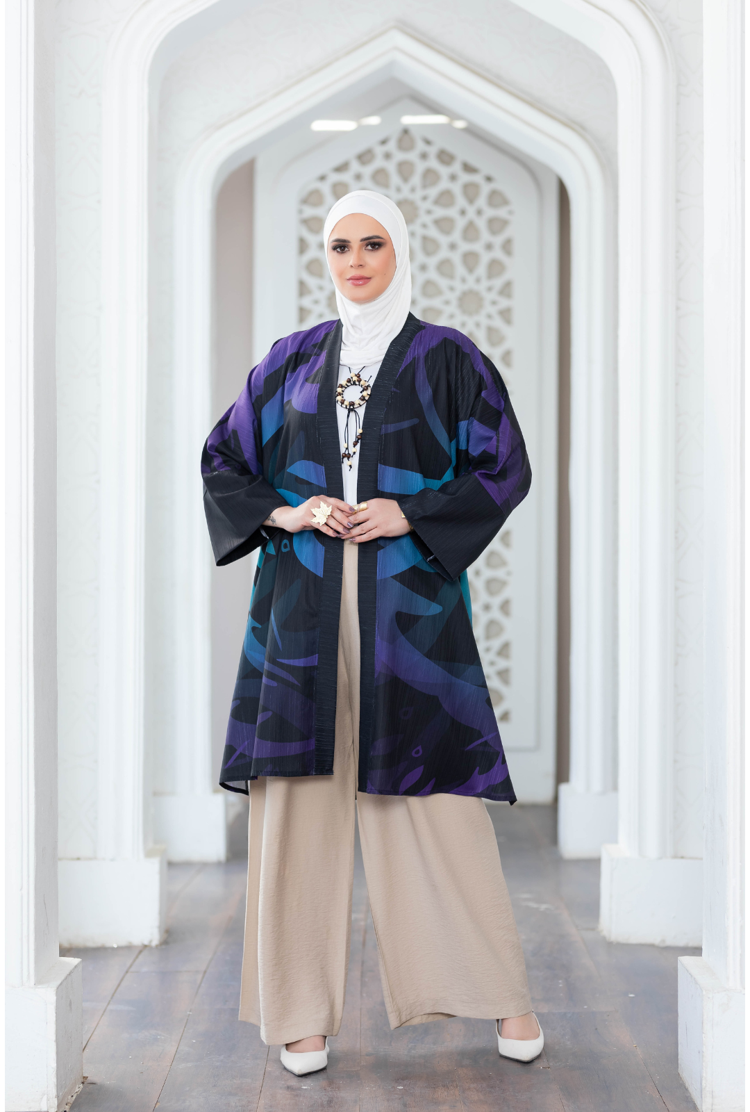 Vibrant floral-patterned kimono worn by woman in traditional Islamic attire posing inside a modern architectural setting.