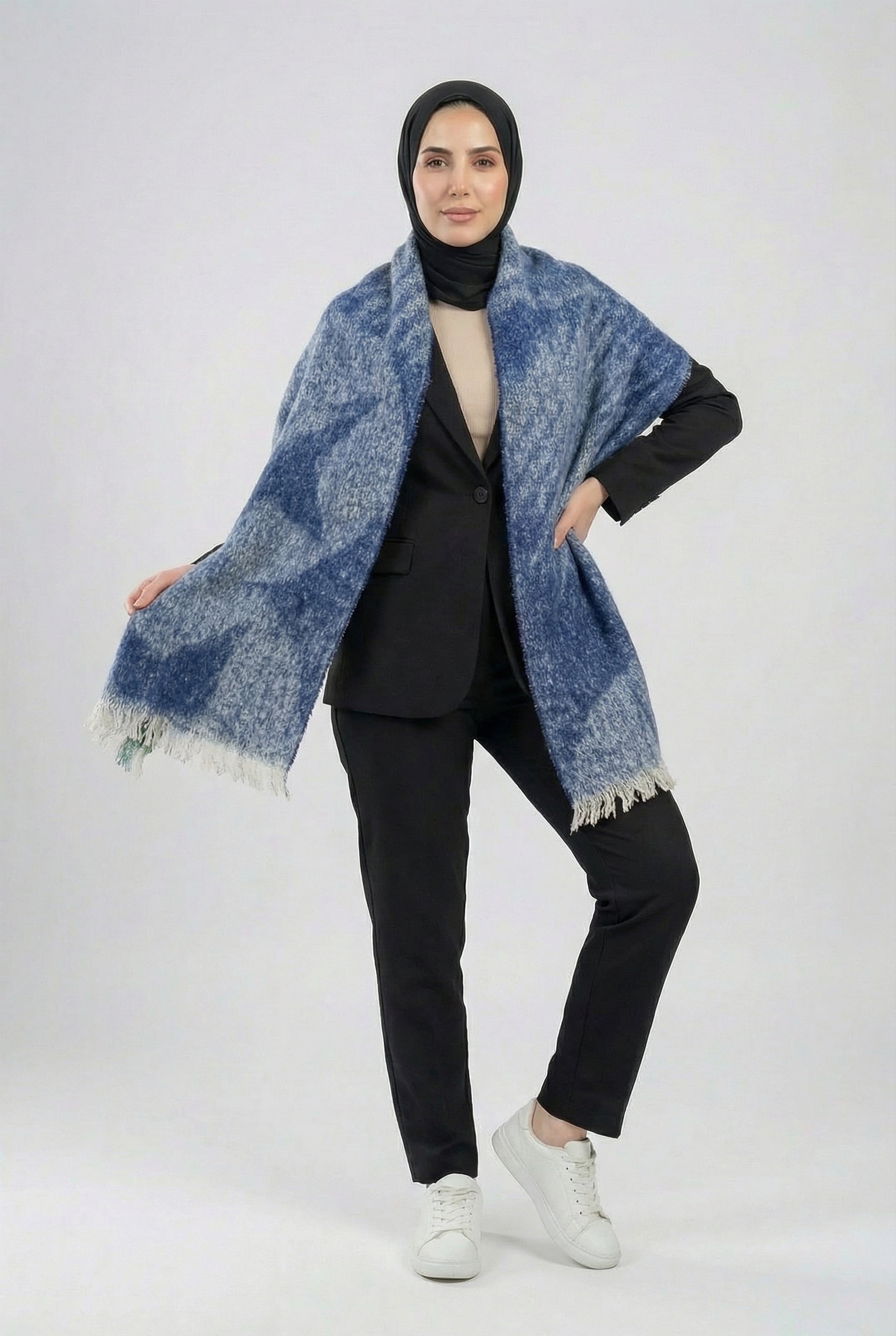 Woman wearing a blue patterned shawl over a black outfit on a white background