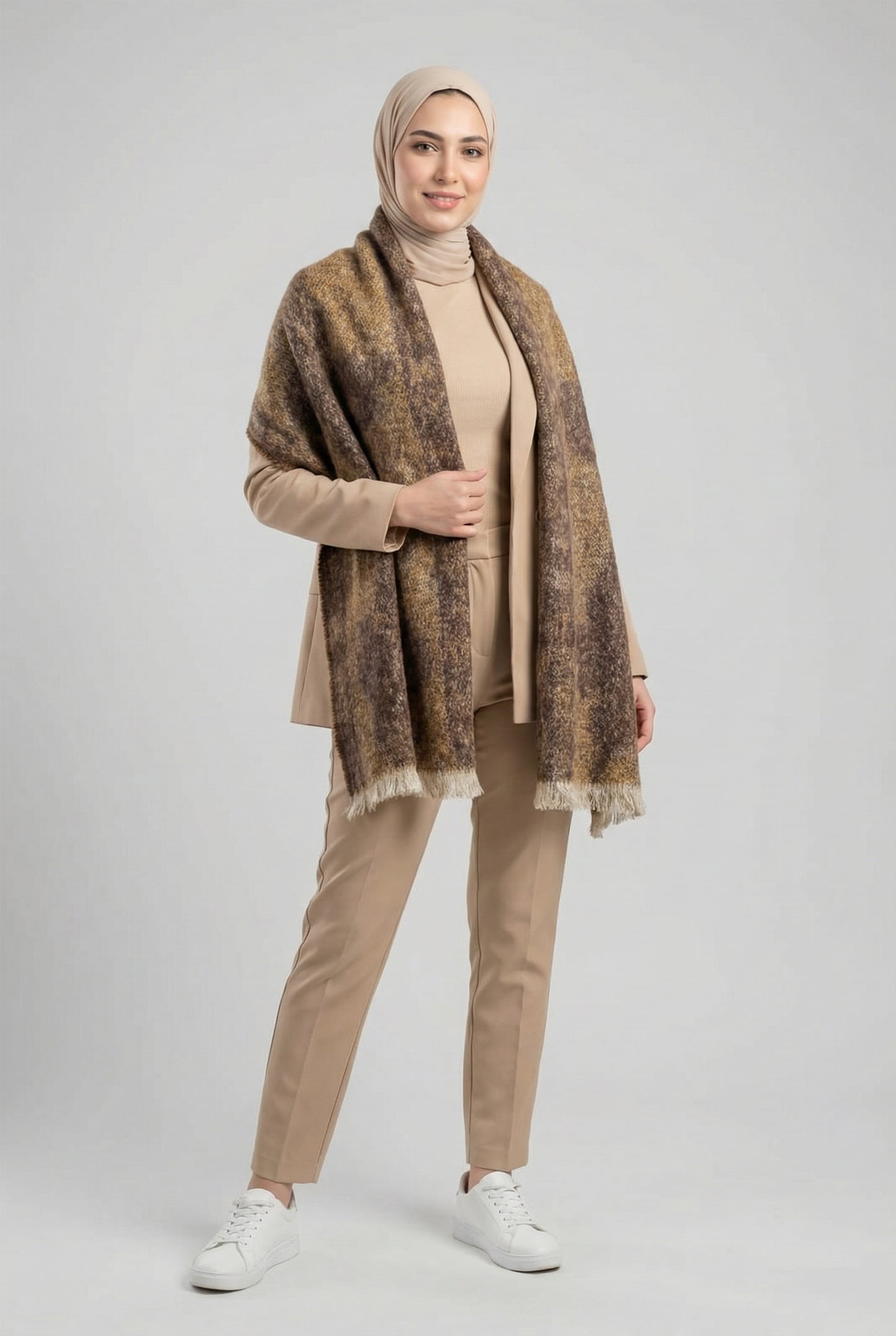 Woman wearing a patterned shawl, beige top, pants, and white shoes on a light gray background