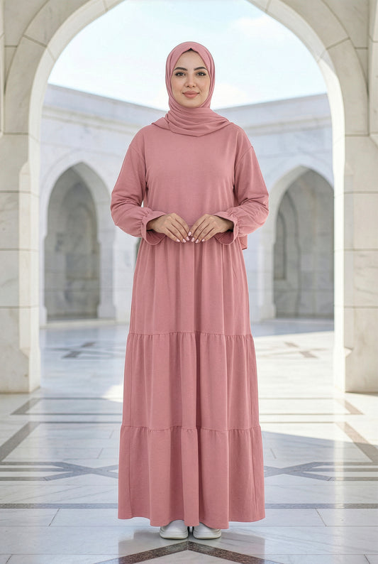 Model wearing a dusty rose Aura Isdal with a flowing tiered silhouette in an elegant outdoor courtyard.