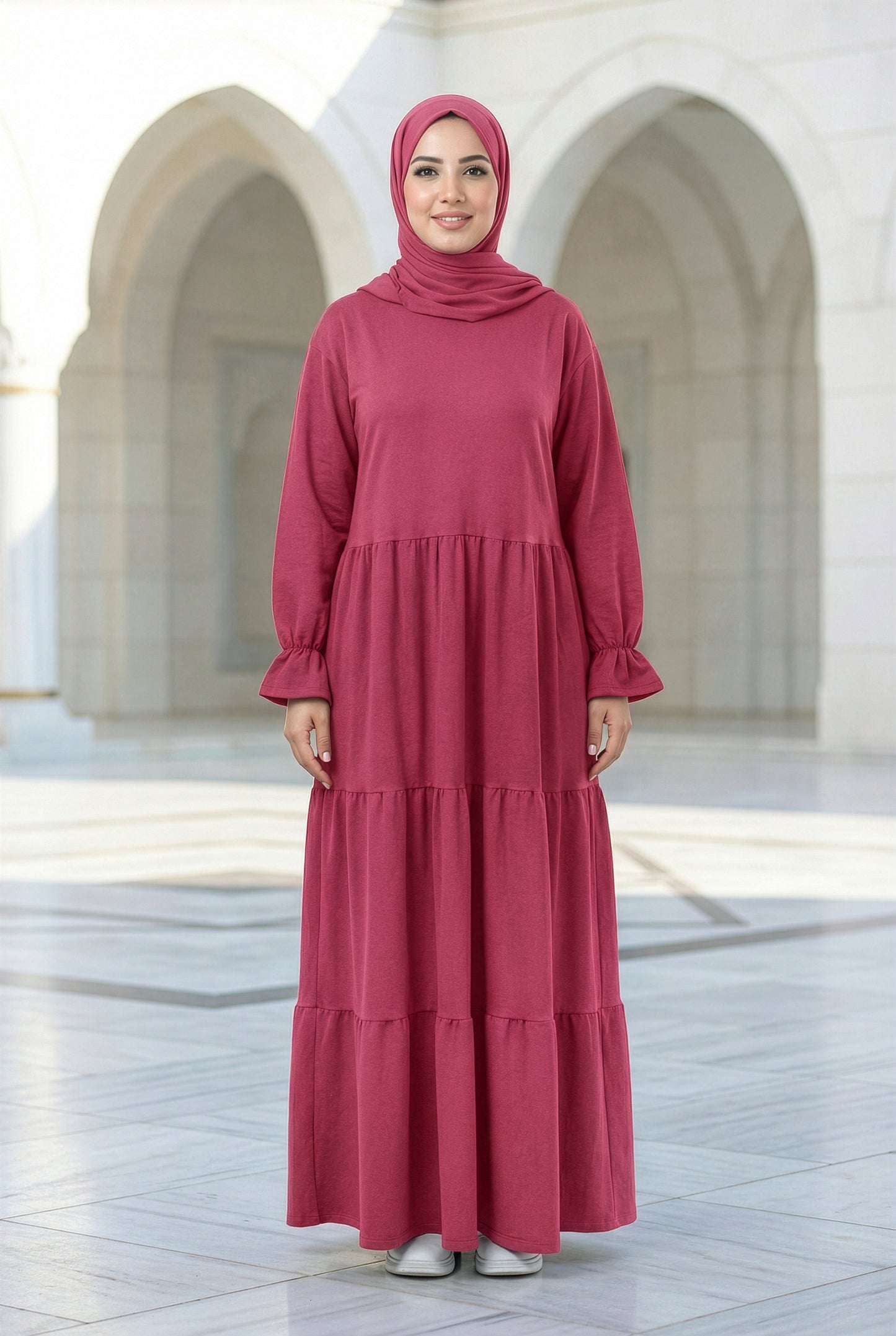 Model wearing a raspberry pink Aura Isdal with a flowing tiered silhouette in an outdoor architectural courtyard