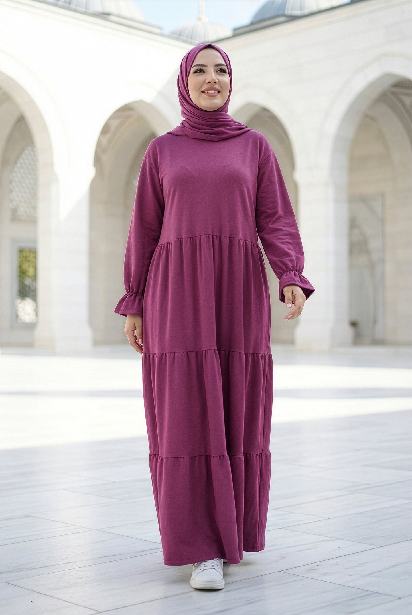 Model wearing a dark fuchsia Aura Isdal with a flowing tiered silhouette in an elegant outdoor courtyard