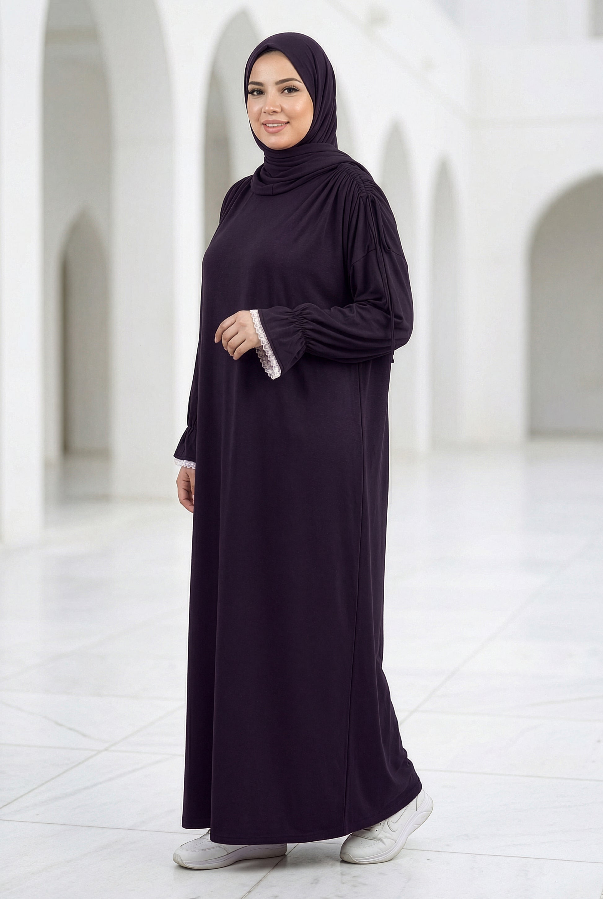 Woman wearing a deep plum Grace Isdal with white embroidered cuffs, modest full-length abaya photographed in a bright white arched hallway