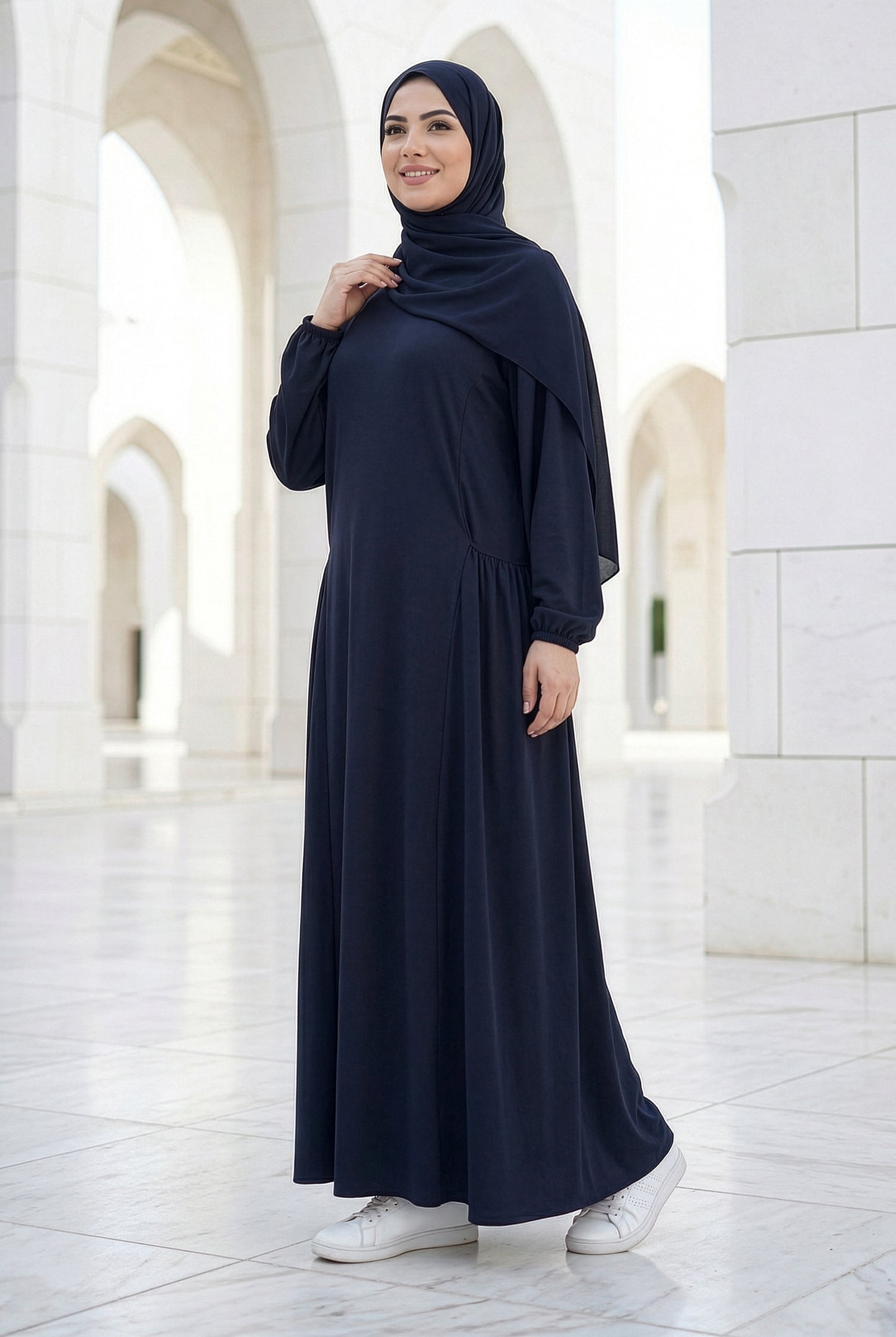 Woman wearing a deep navy Royale Isdal, modest flowing abaya with lightweight fabric photographed in a bright white marble courtyard