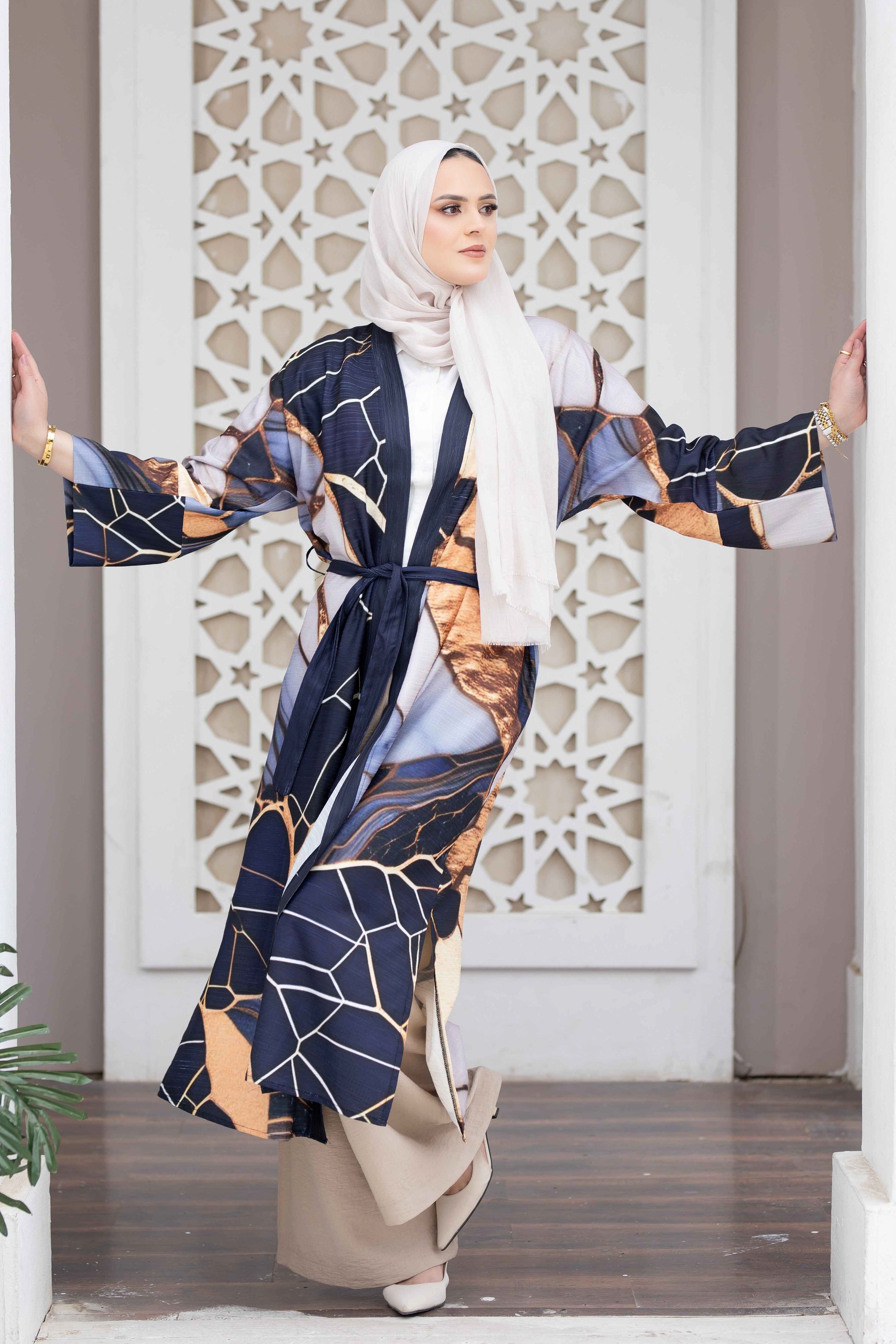 Elegant digital print kimono in navy and beige, featuring intricate geometric patterns and flowing sleeves, worn by a model in front of a decorative archway.