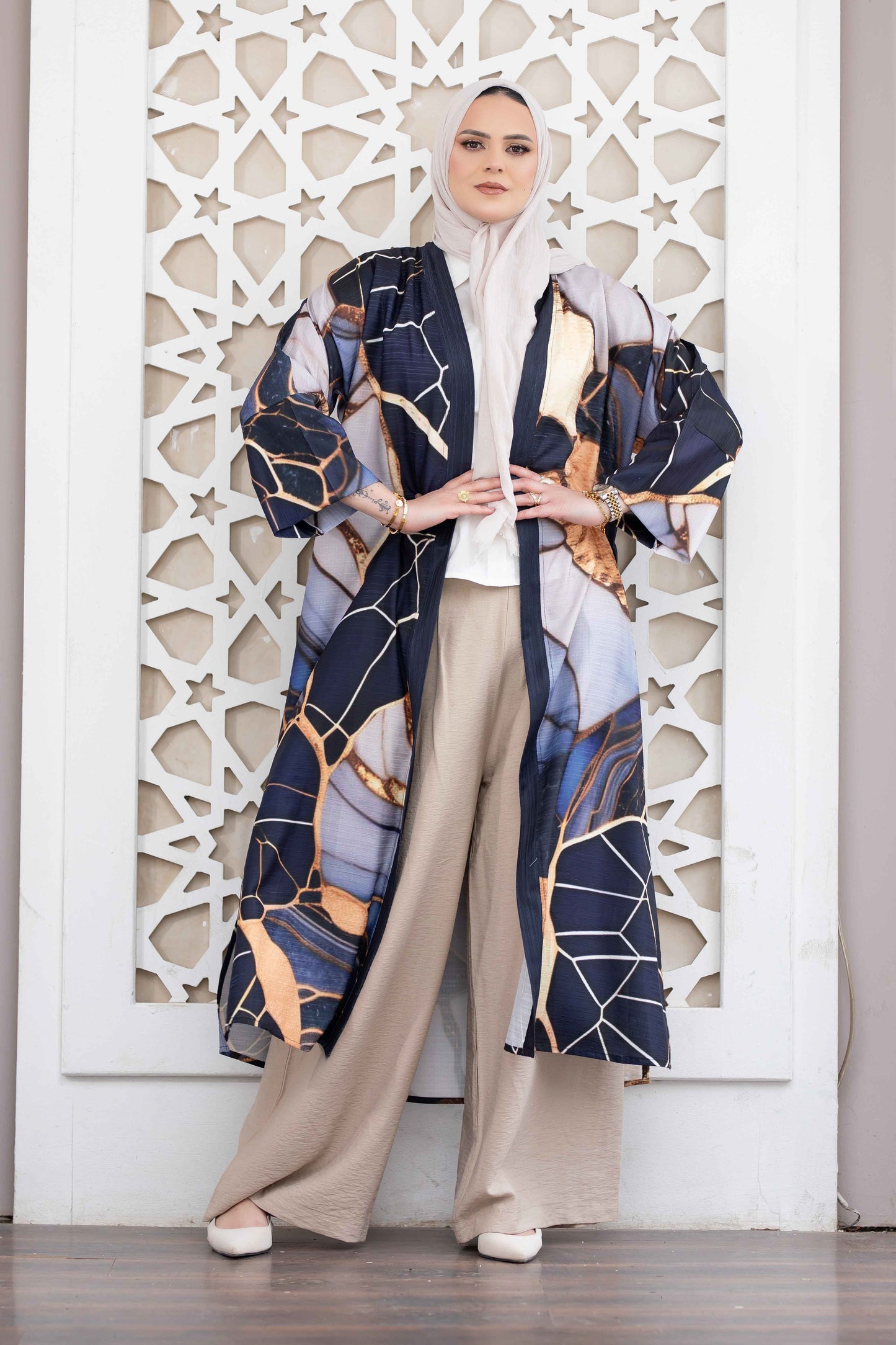 Digital print kimono with abstract geometric pattern in shades of blue, orange, and white. Worn by a woman with a hijab standing in front of a decorative white wall.