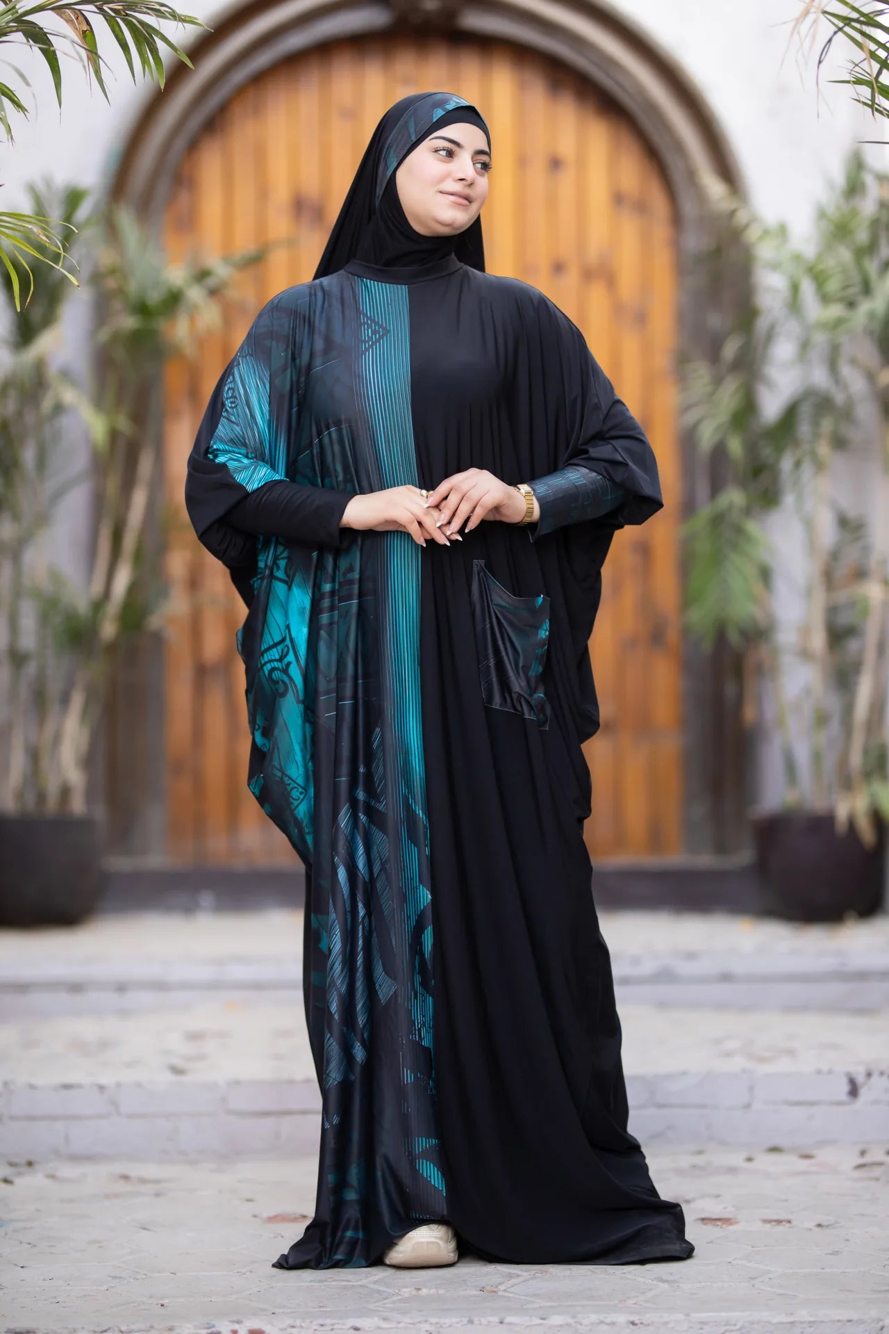 Woman wearing a black abaya with a blue pattern in an outdoor setting.