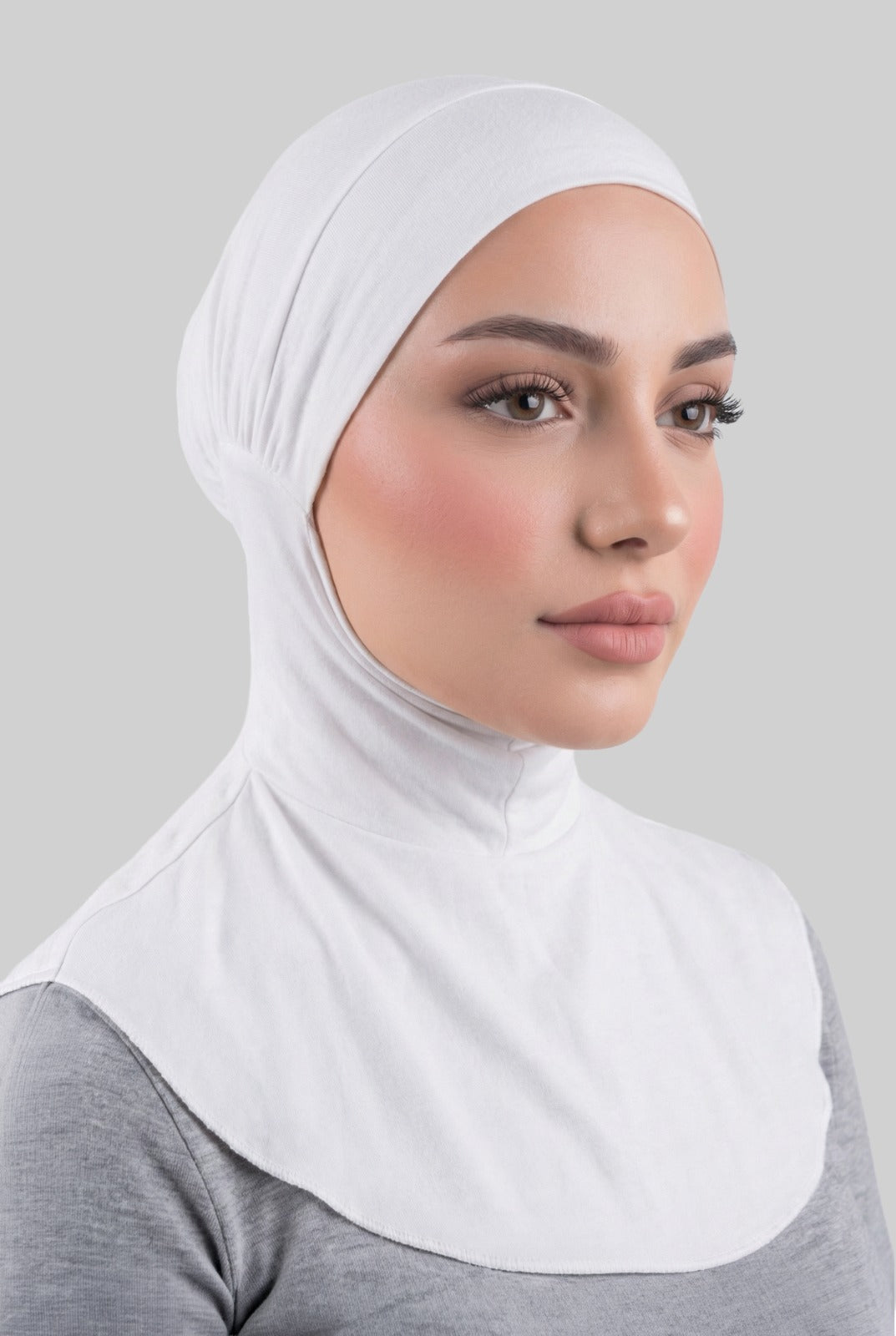 Woman wearing a white hijab against a gray background