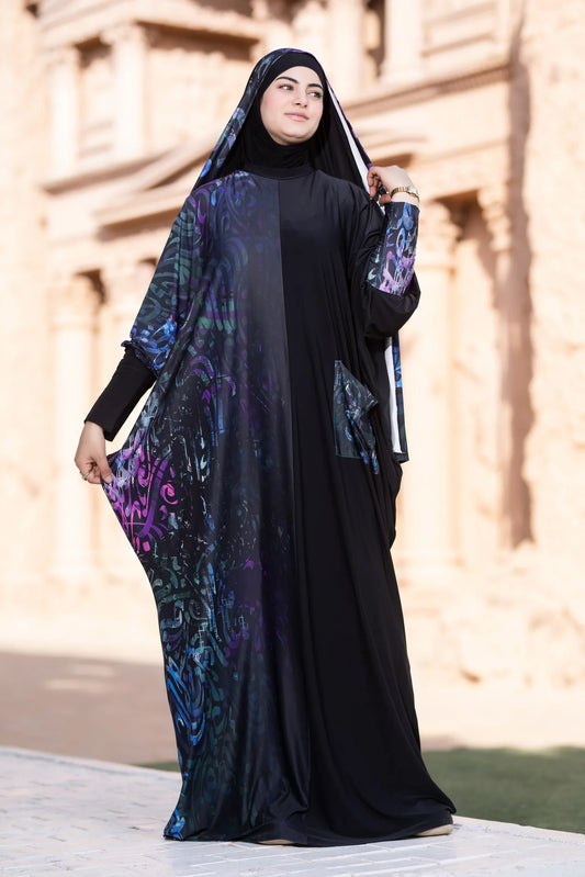 Woman wearing a black abaya with colorful patterns outdoors.