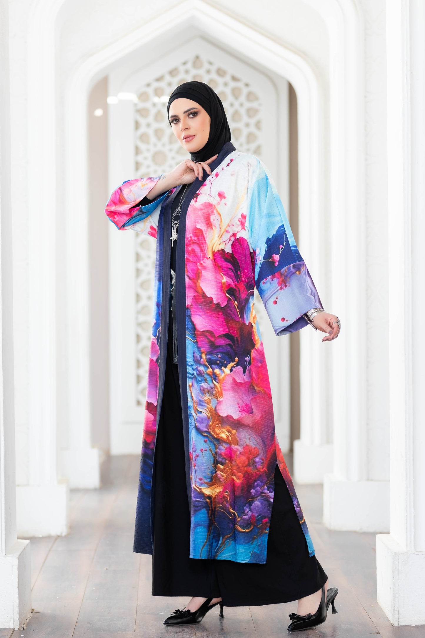 Elegant floral digital print kimono with vibrant colors and patterns, worn by a woman in a traditional Islamic headscarf, standing in an ornate architectural setting.