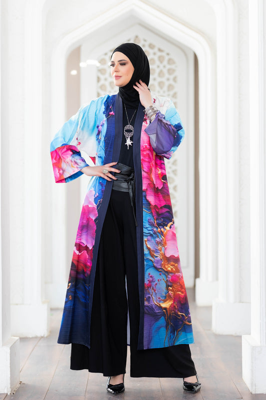 Vibrant floral print digital kimono with long sleeves and open front, worn over a black outfit with decorative pendant, against a white architectural background.