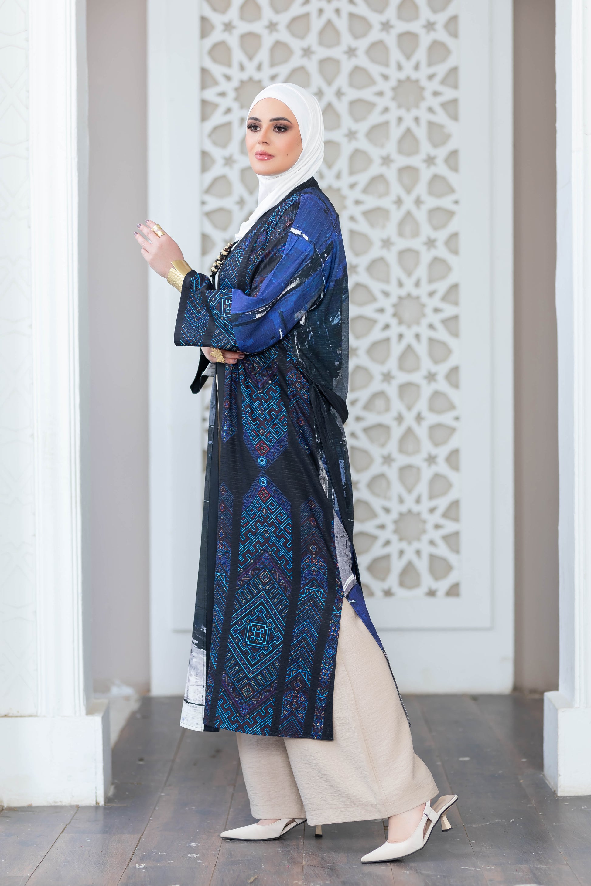Elegant digital print kimono with intricate blue and teal patterns, worn by a person standing in front of a decorative white architectural backdrop.