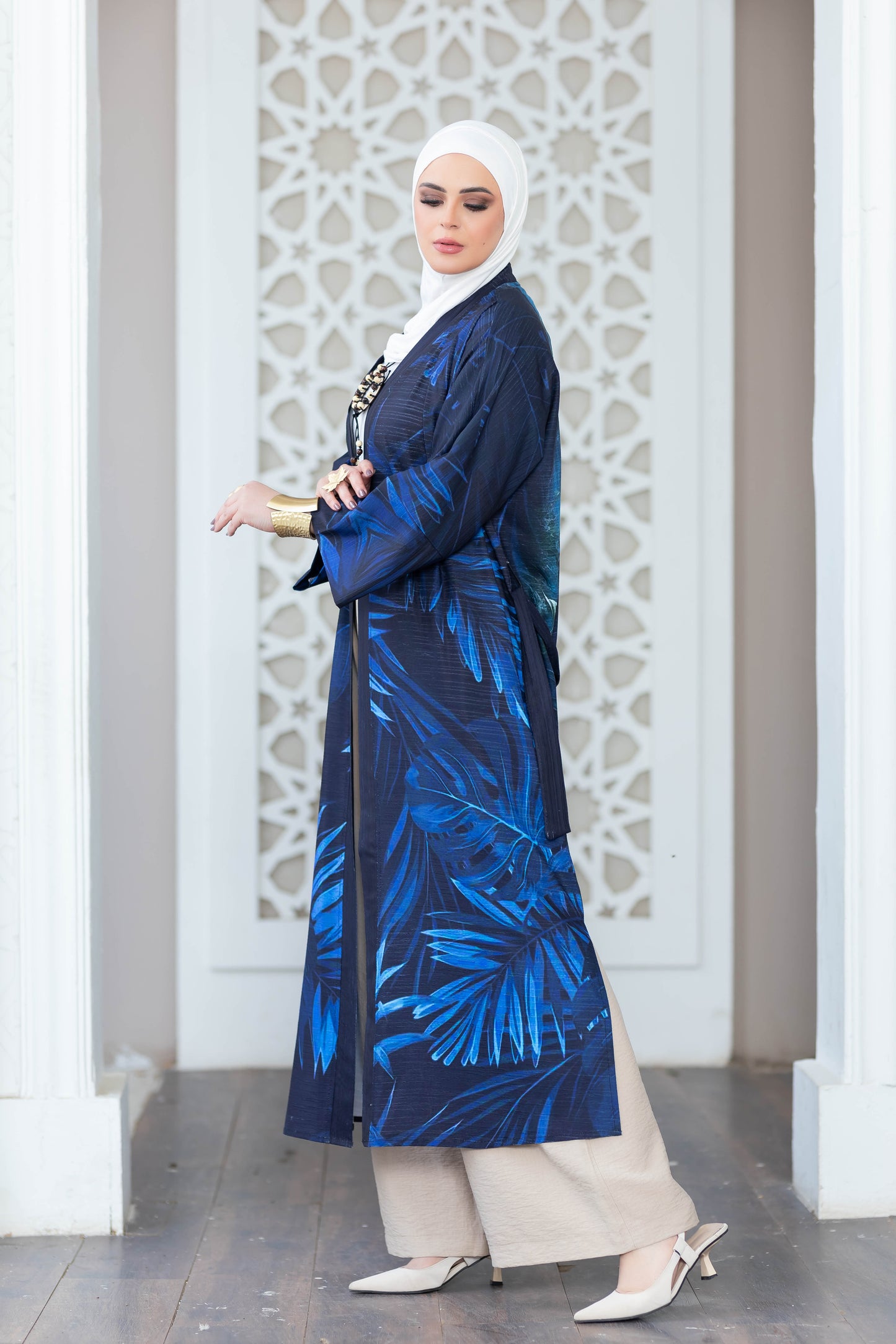 Elegant digital print kimono with vibrant blue and white palm leaf motif, worn by a woman with hijab against a decorative white architectural backdrop.