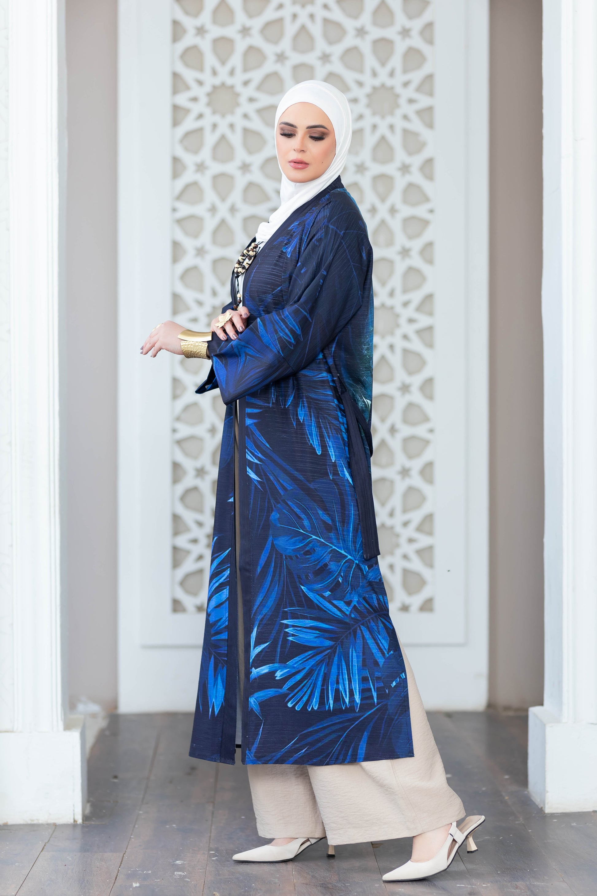 Elegant digital print kimono with vibrant blue and white palm leaf motif, worn by a woman with hijab against a decorative white architectural backdrop.