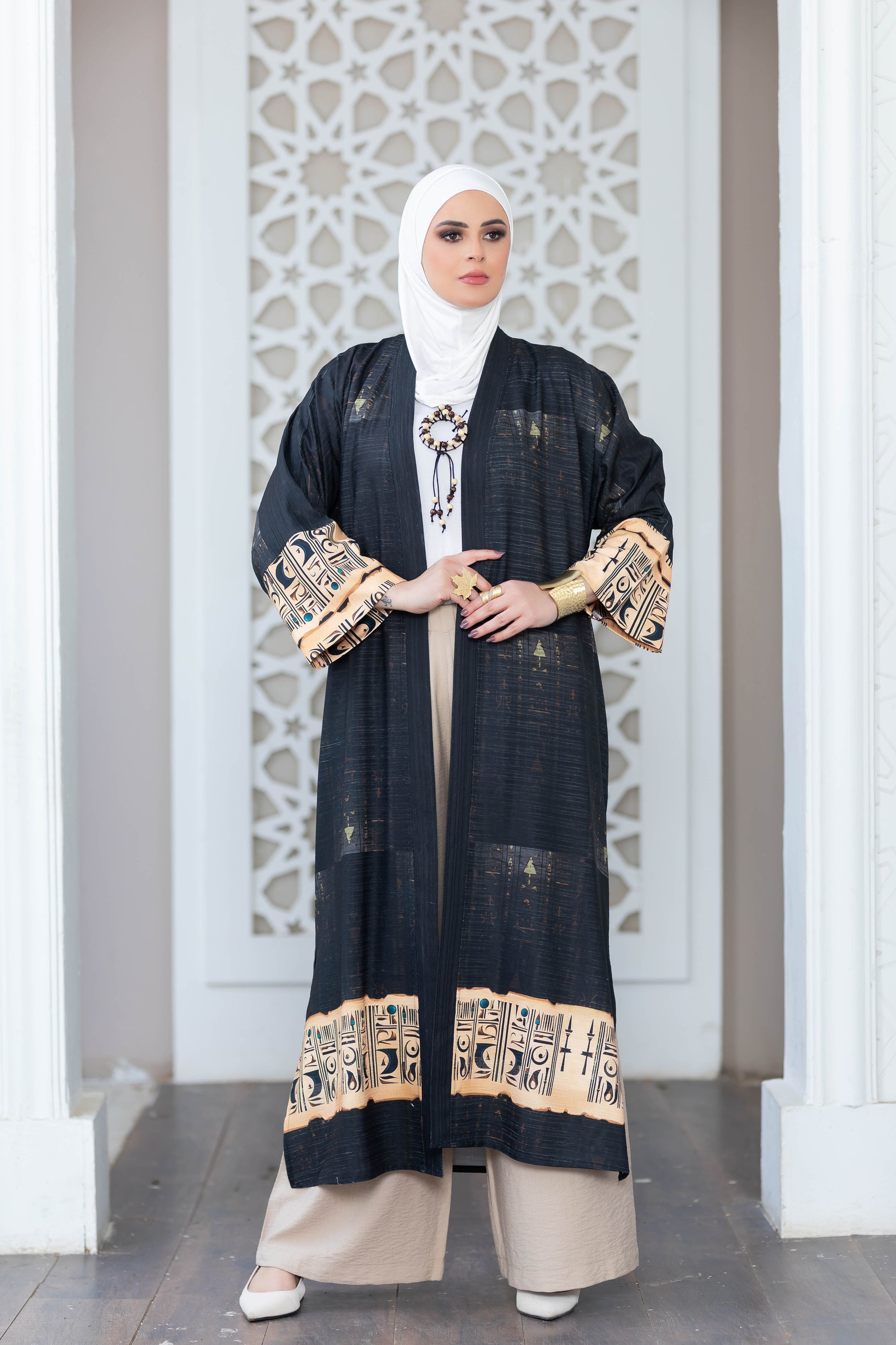 Elegantly patterned black kimono with gold accents, worn by a woman against a traditional Islamic architectural backdrop.
