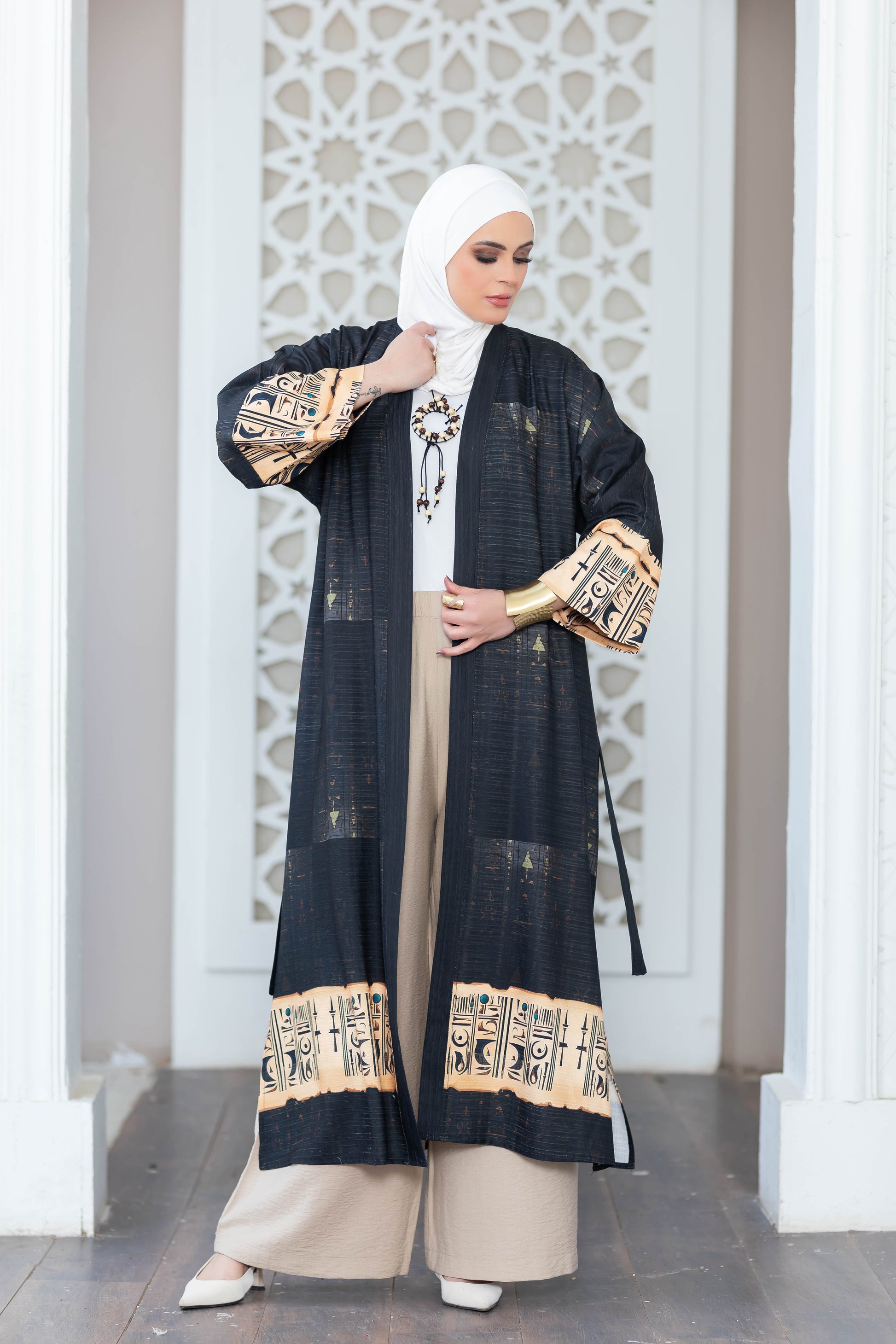 Digital print black kimono with geometric patterns and beige accents, worn by a woman standing in front of a white patterned wall.