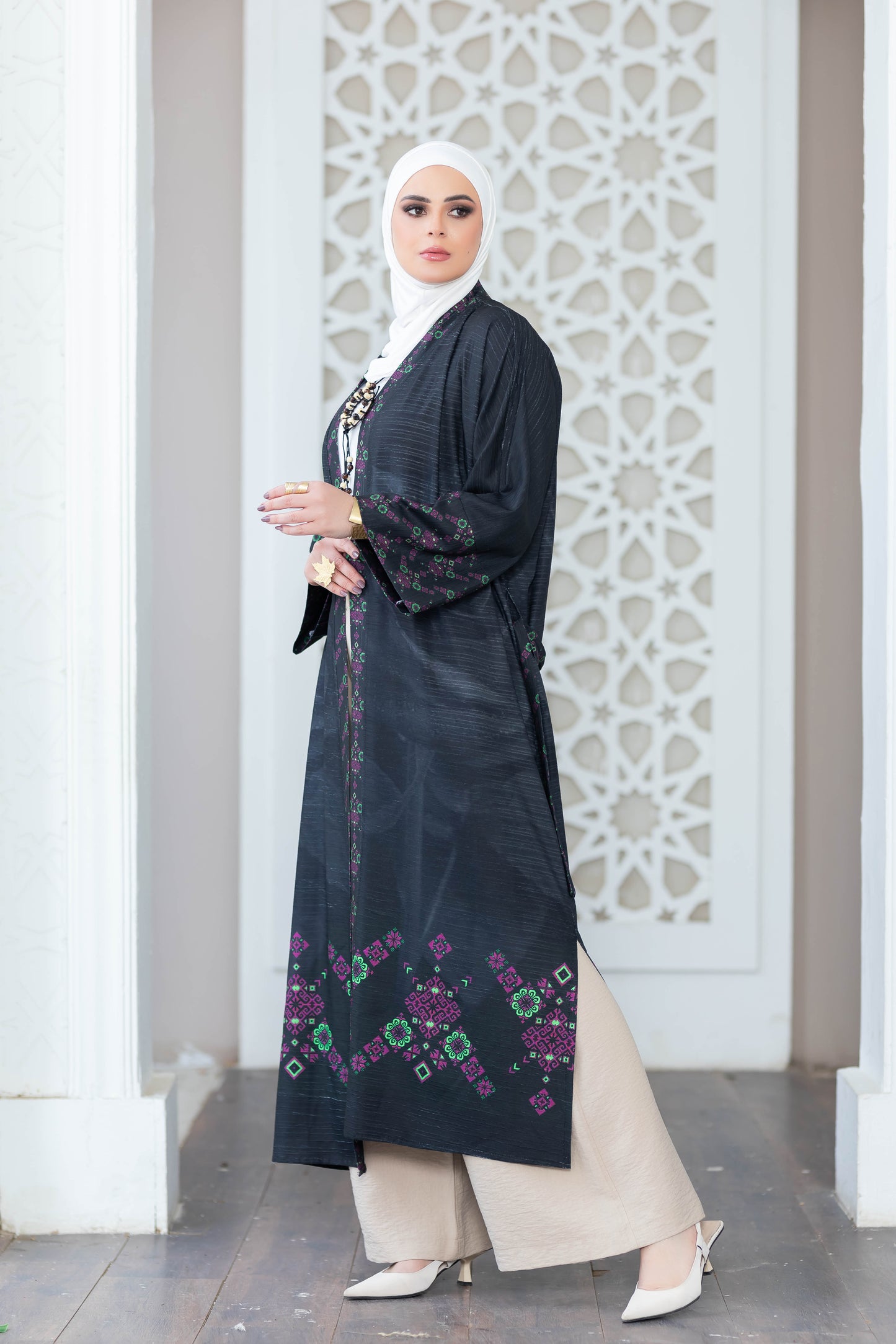 Elegant Islamic floral print abaya with patterned panels, worn by a woman standing in front of ornamental white archway.