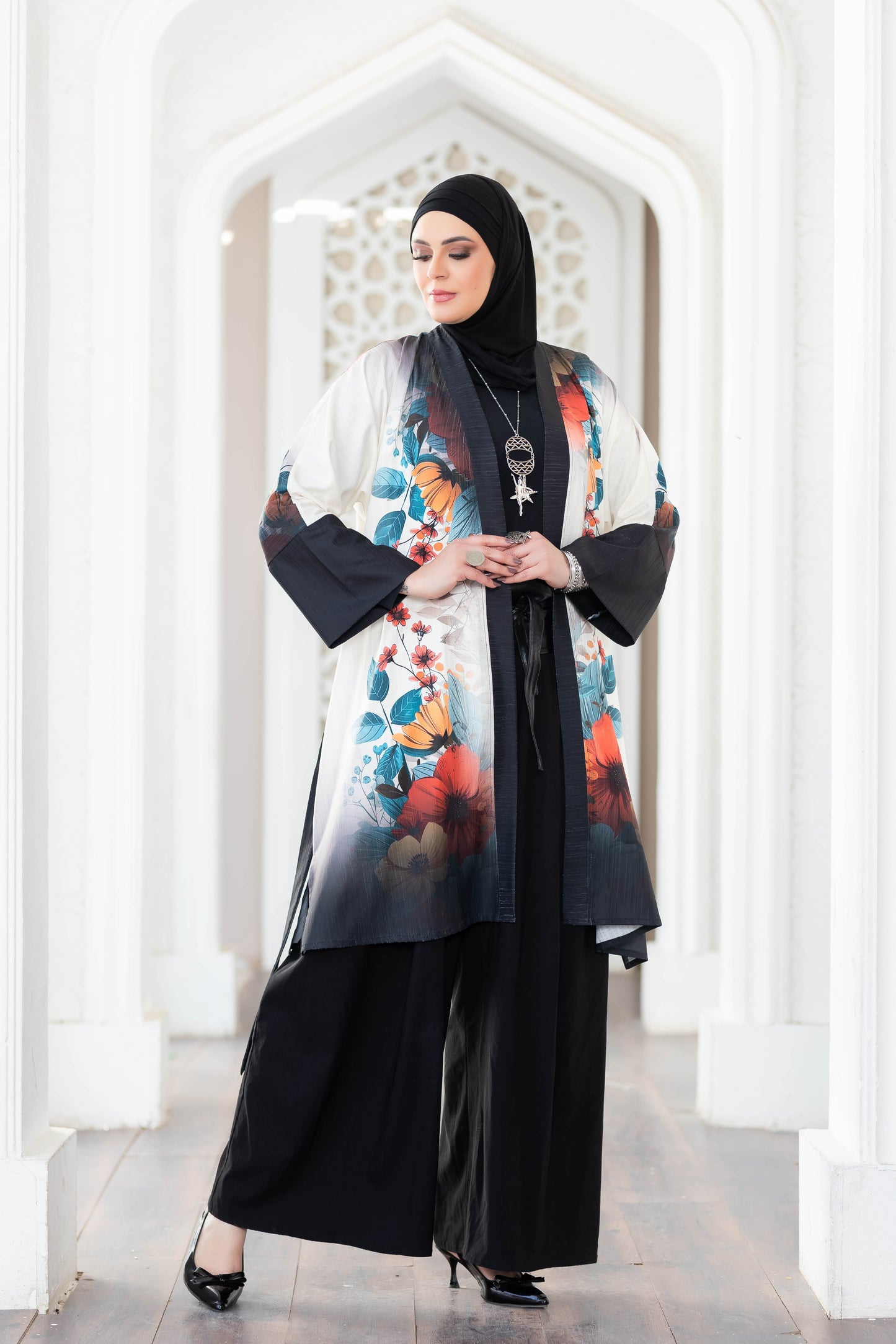 Vibrant floral-printed kimono with long bell sleeves, worn by a woman in traditional hijab, standing in an ornate architectural setting.