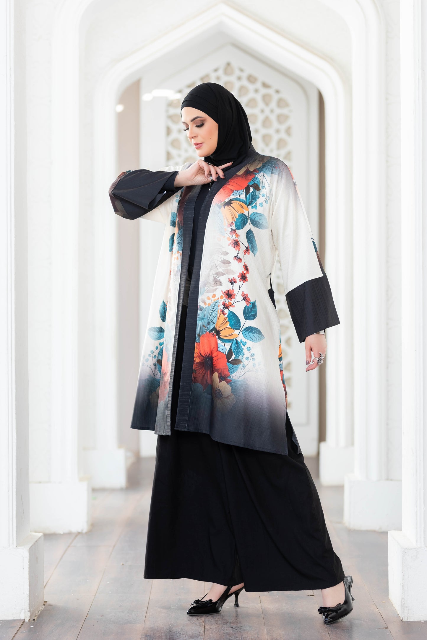 Floral patterned mid-length kimono with black trim, worn over a black outfit by a woman in a white hallway.
