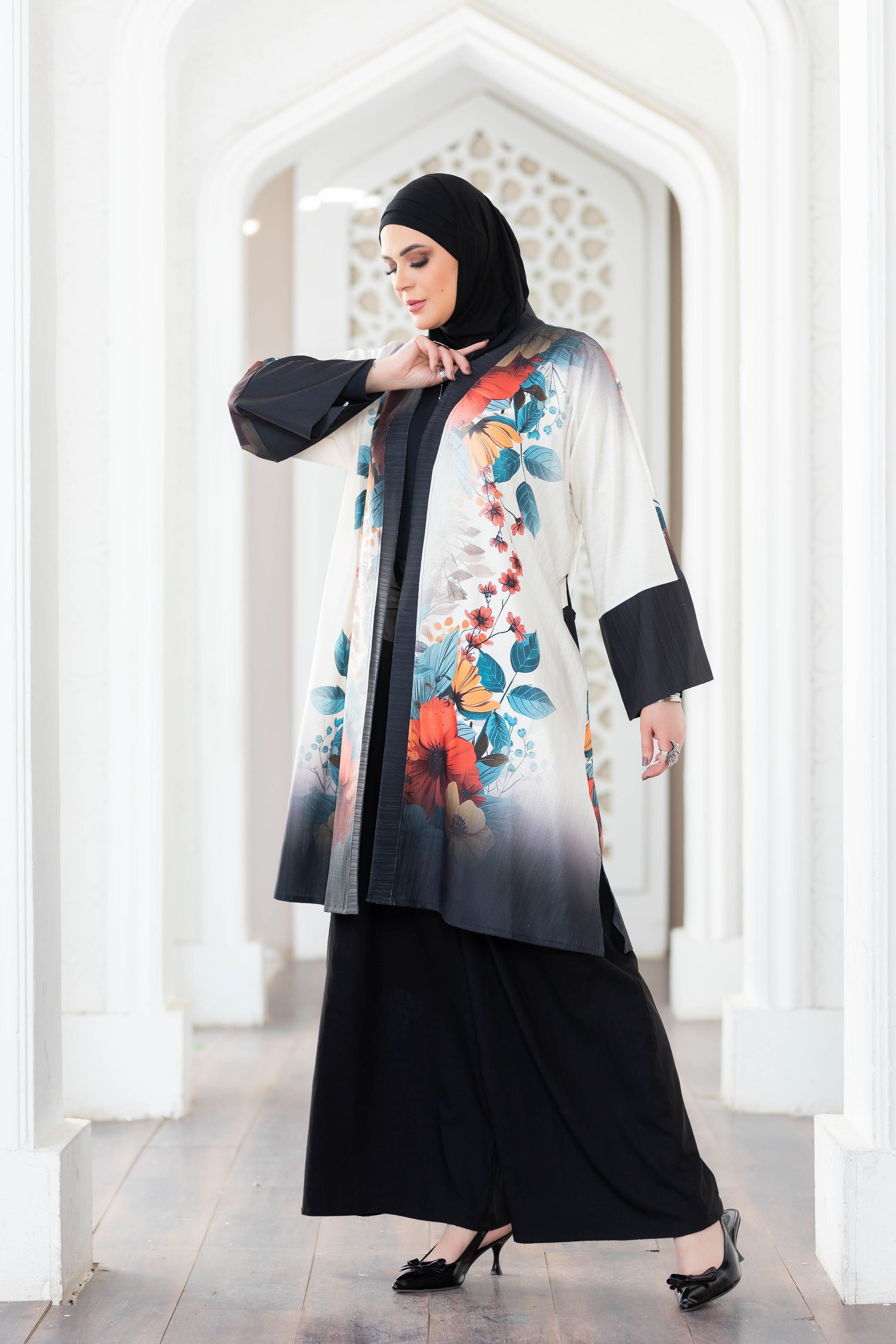 Floral patterned mid-length kimono with black trim, worn over a black outfit by a woman in a white hallway.