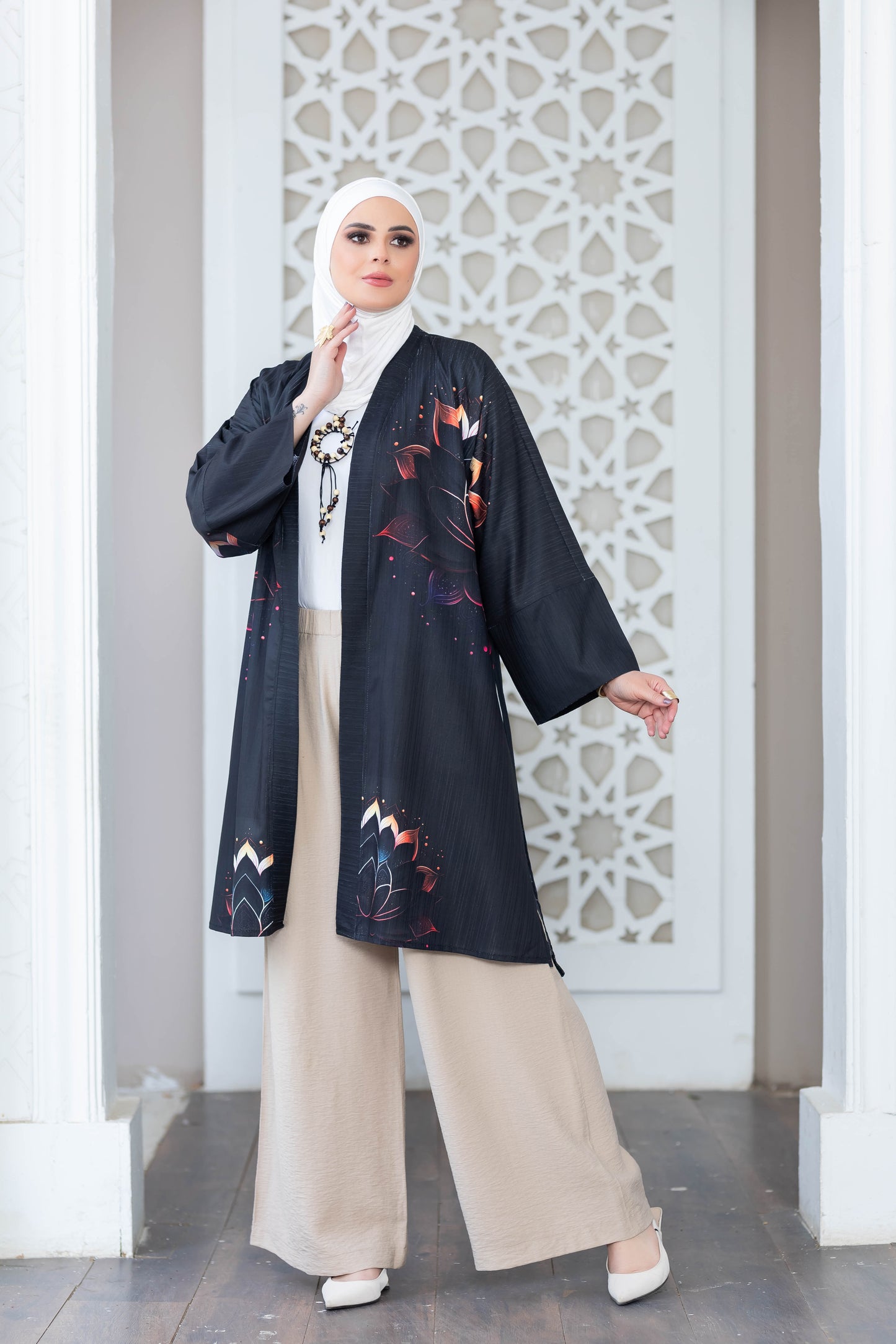 Elegant floral patterned black kimono with long sleeves, worn over beige trousers, showcased against an intricate white backdrop.