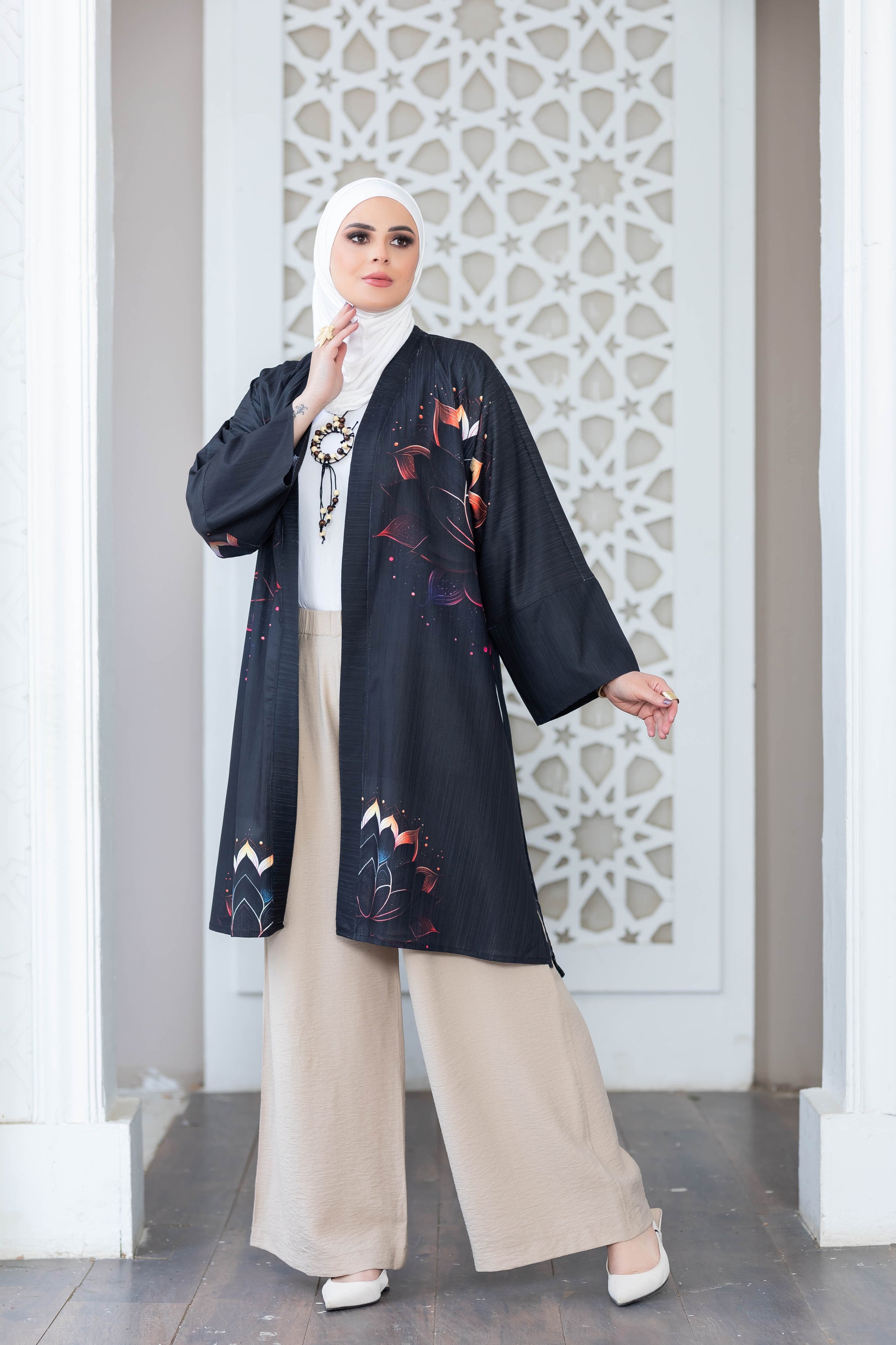 Elegant floral patterned black kimono with long sleeves, worn over beige trousers, showcased against an intricate white backdrop.