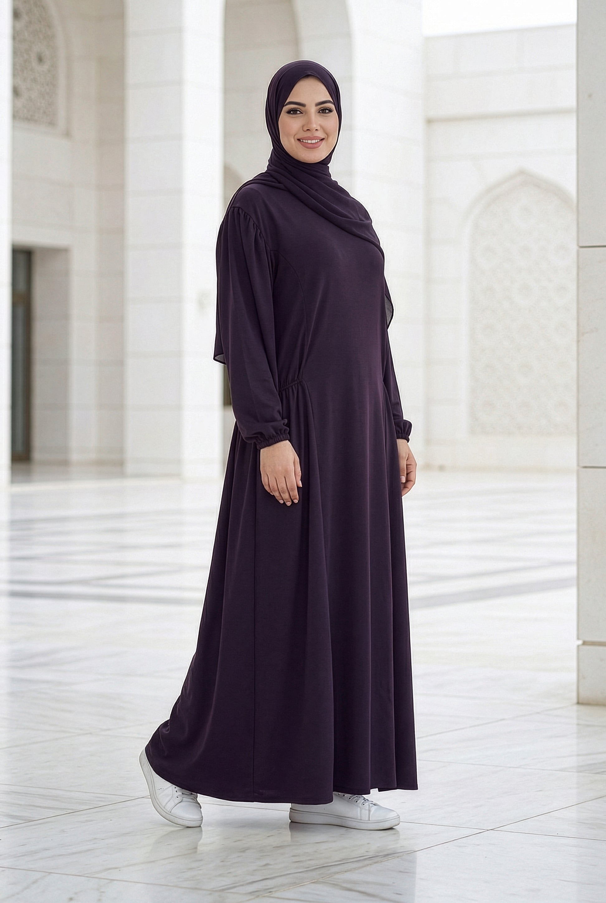 Model wearing a deep plum Royale Isdal with a flowing modest design in a bright architectural courtyard