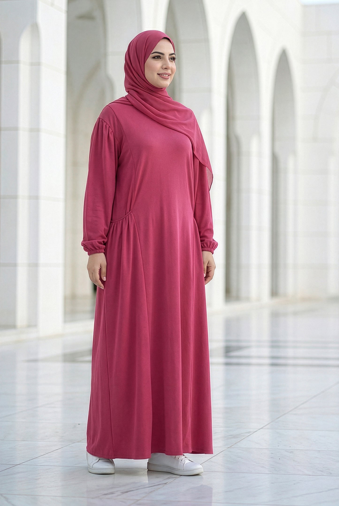 Model wearing a raspberry pink Royale Isdal with a flowing modest silhouette in a bright architectural courtyard